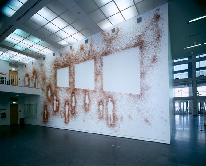 A mural that covers a large wall depicts eleven people and three squares created using orange-brown blow paint.