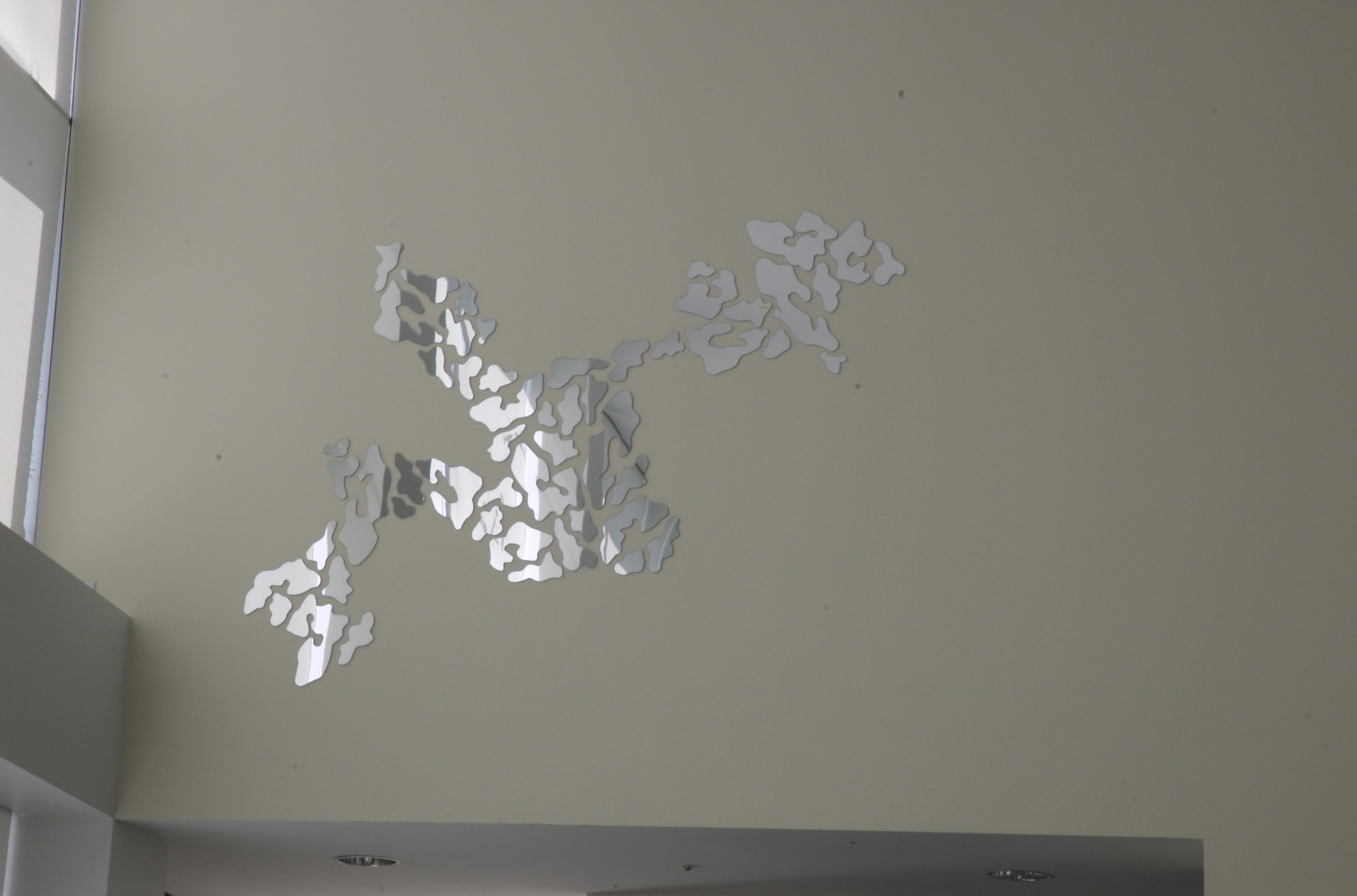Fragmented mirror pieces adhered to a white wall form a jagged shape.