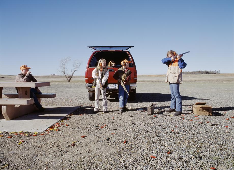 Four people are outdoors, three of whom appear to be children who are holding long-barreled guns.