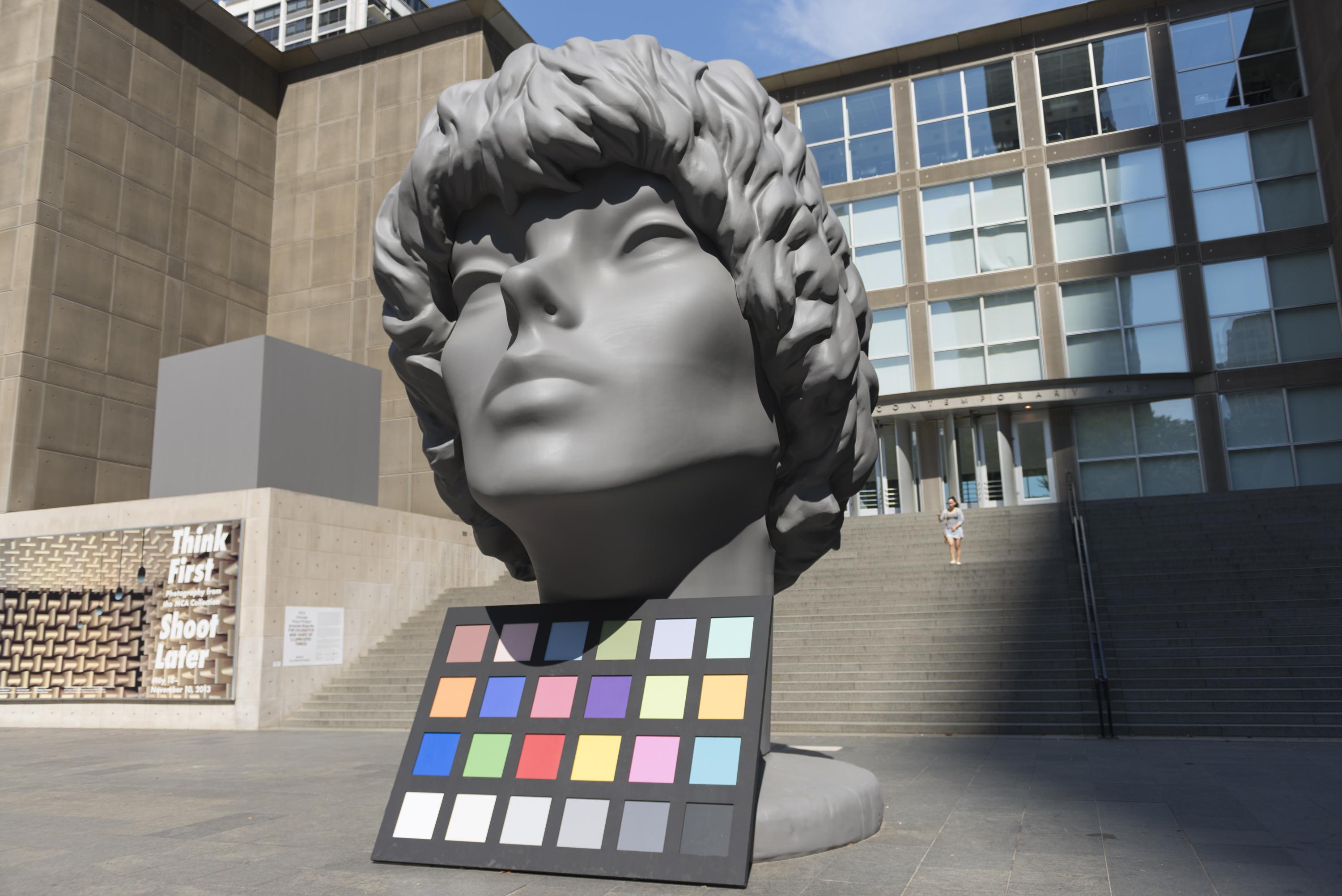 A huge sculpture of person's head is displayed along with a color palette in front of the MCA.