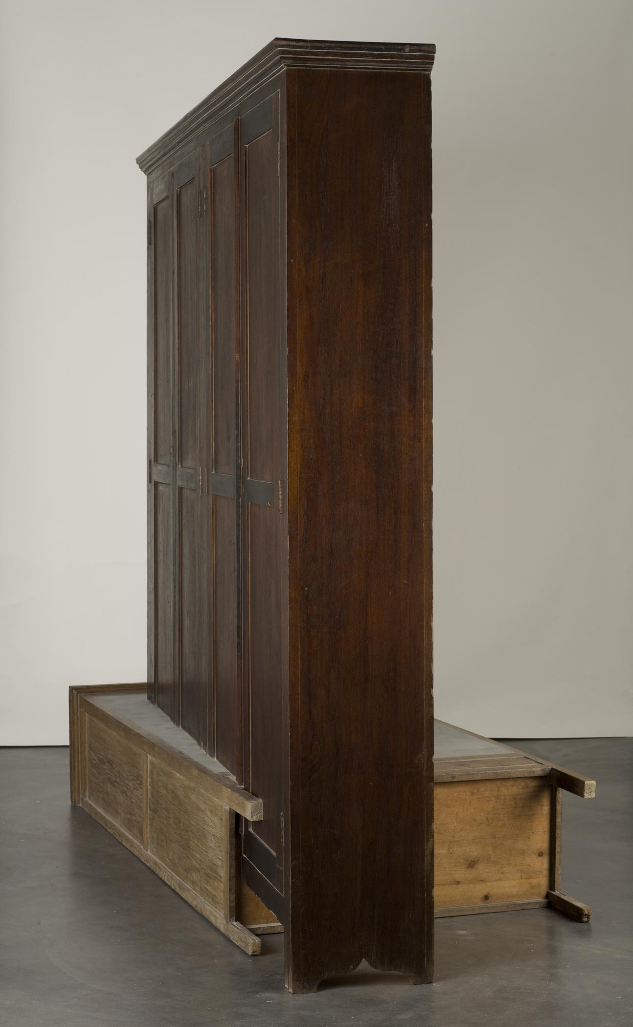 A vertical wooden cabinet precisely intersects a second wooden cabinet laying on the floor.