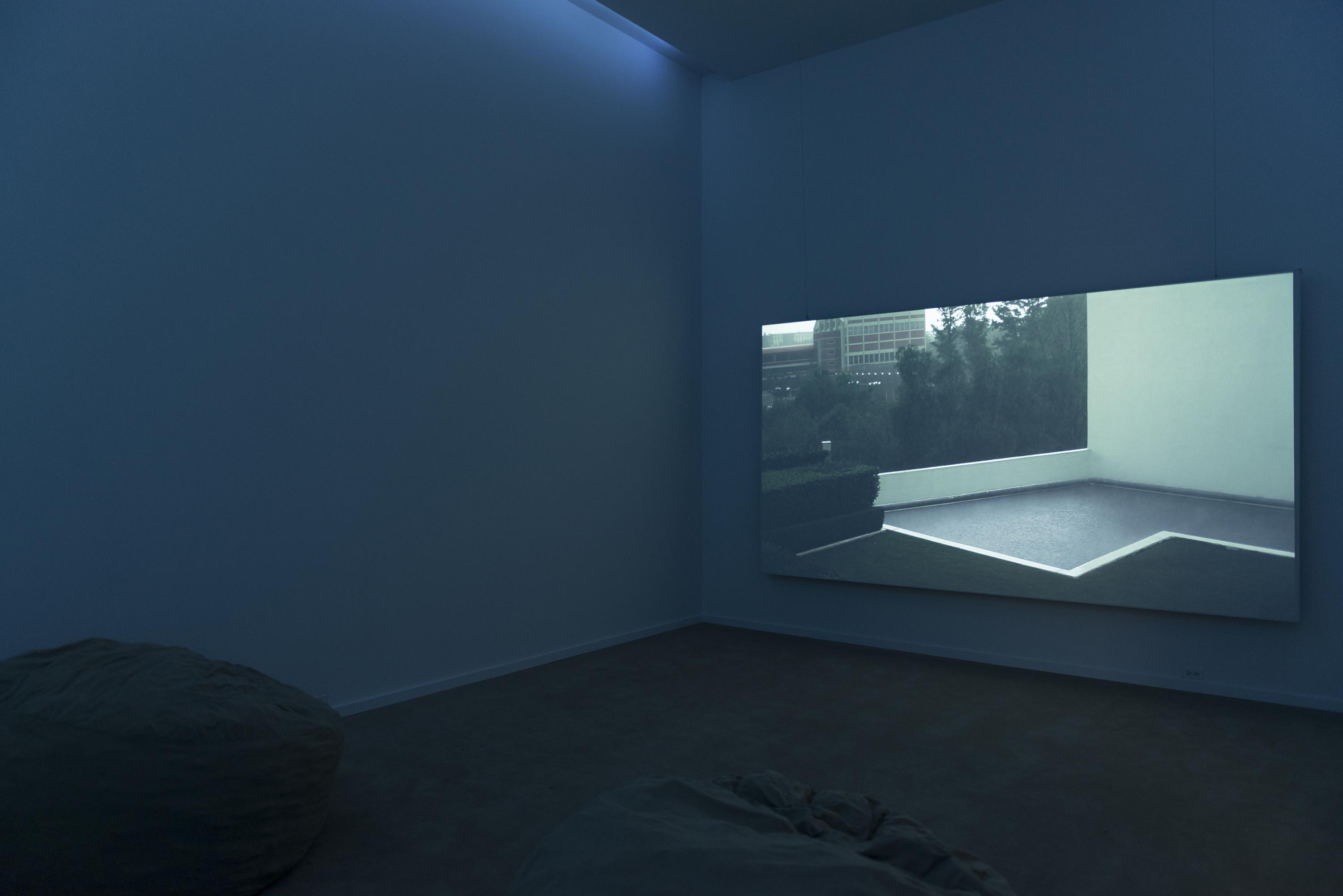 Still of a empty roof terrace projected onto the wall of a dark room with beanbags, just visible on the bottom left.