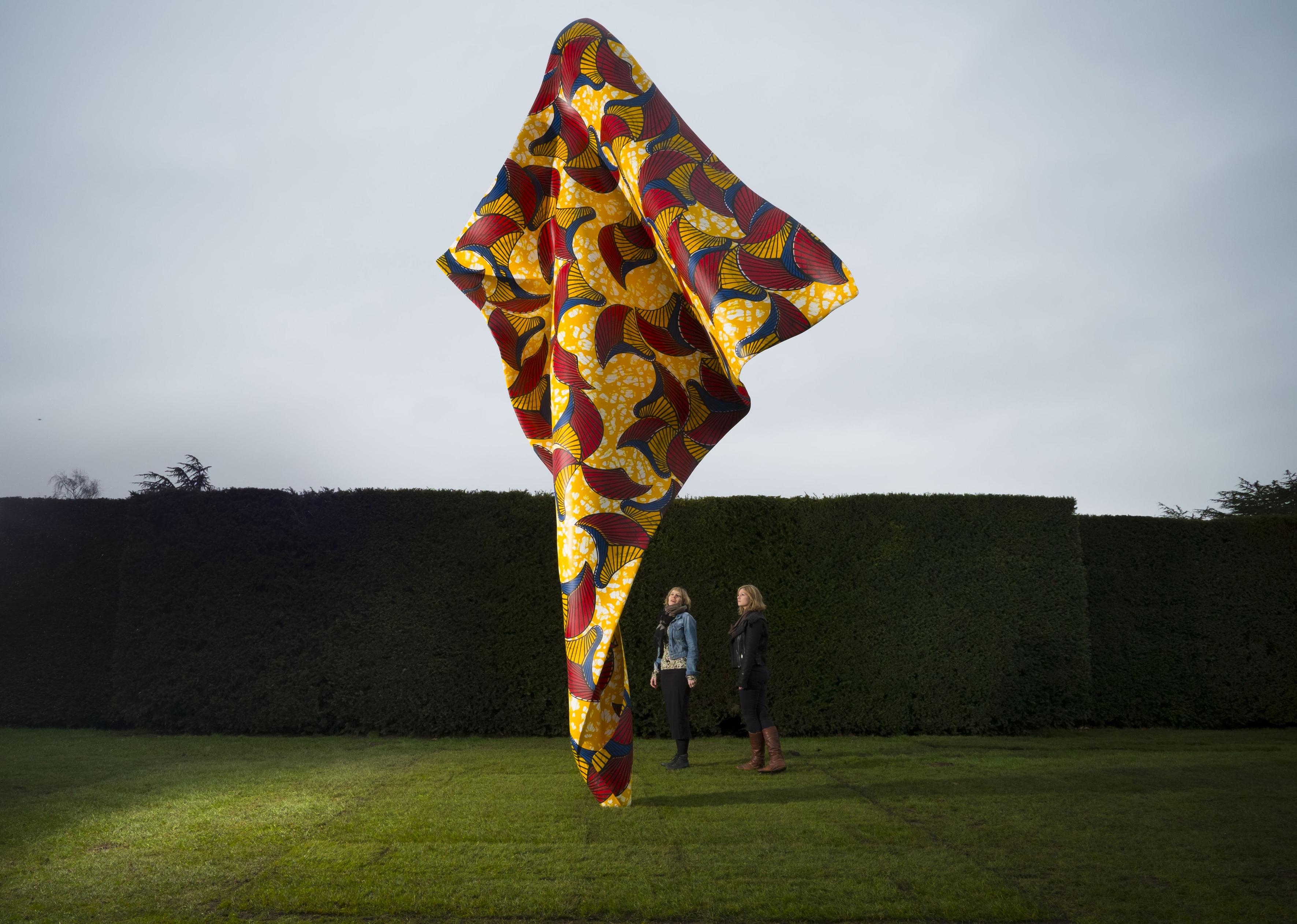 A giant sculpture resembling tussled fabric stands upright in a manicured lawn