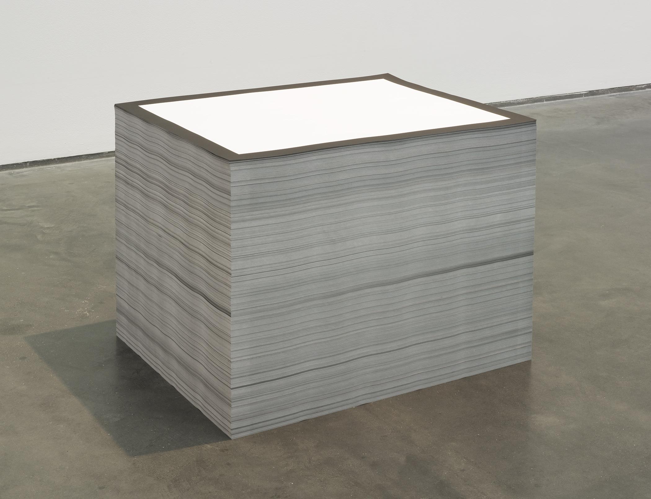 A large and neat stack of white paper with a black border sits on a concrete floor.