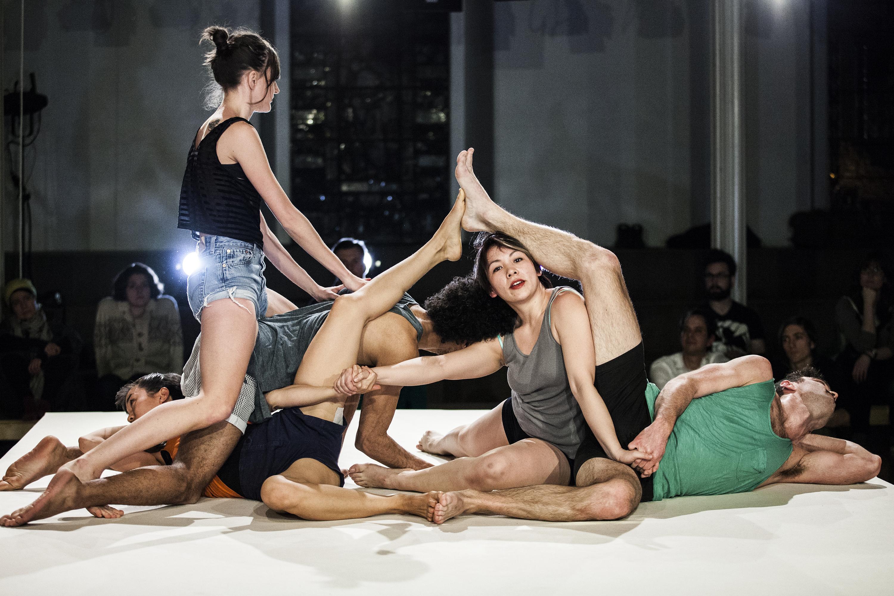 Five coed dancers lie entwined on a small stage