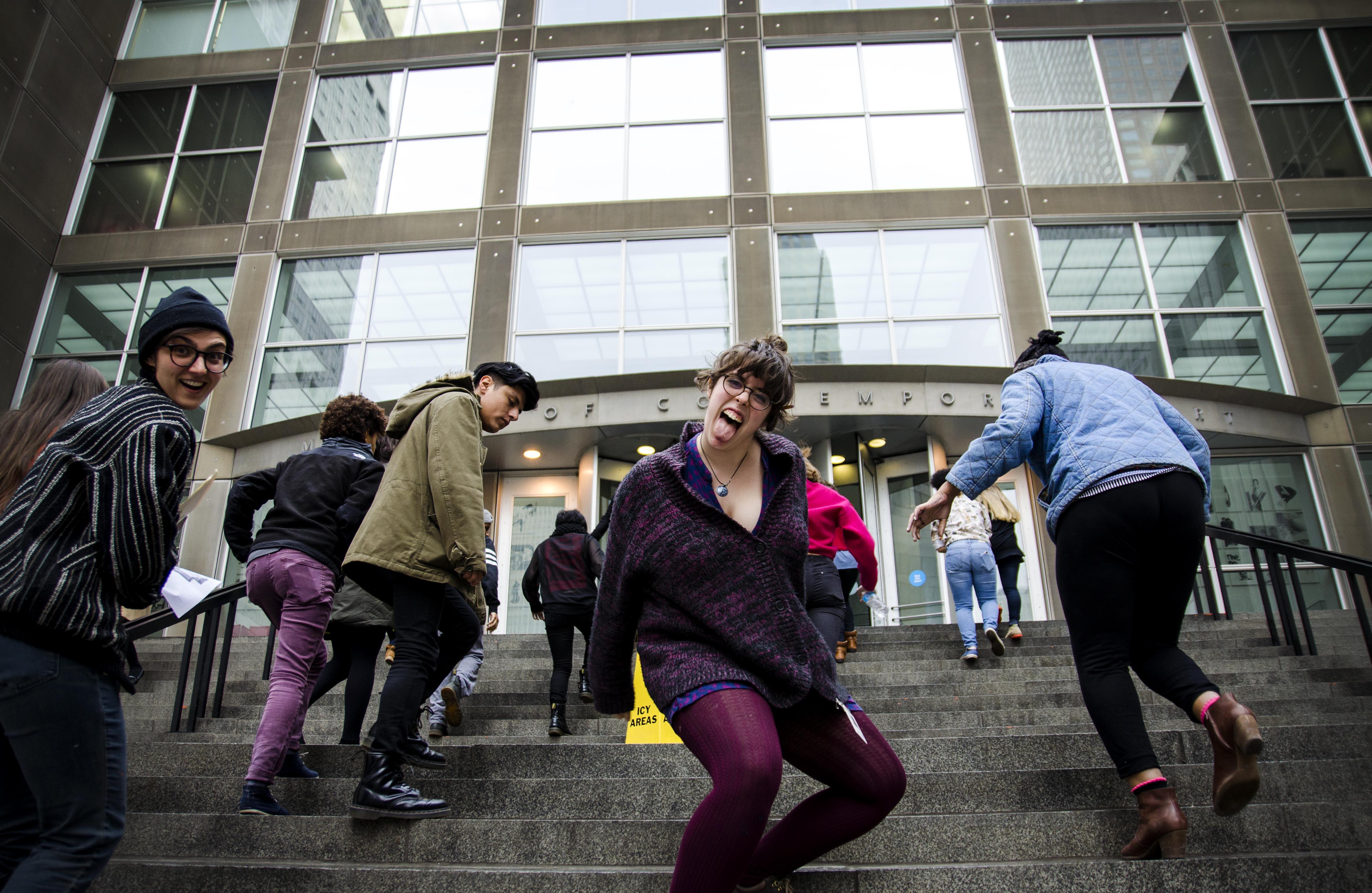 Young adults climb the MCA's front staircase, and two of them turn to make faces at the camera.