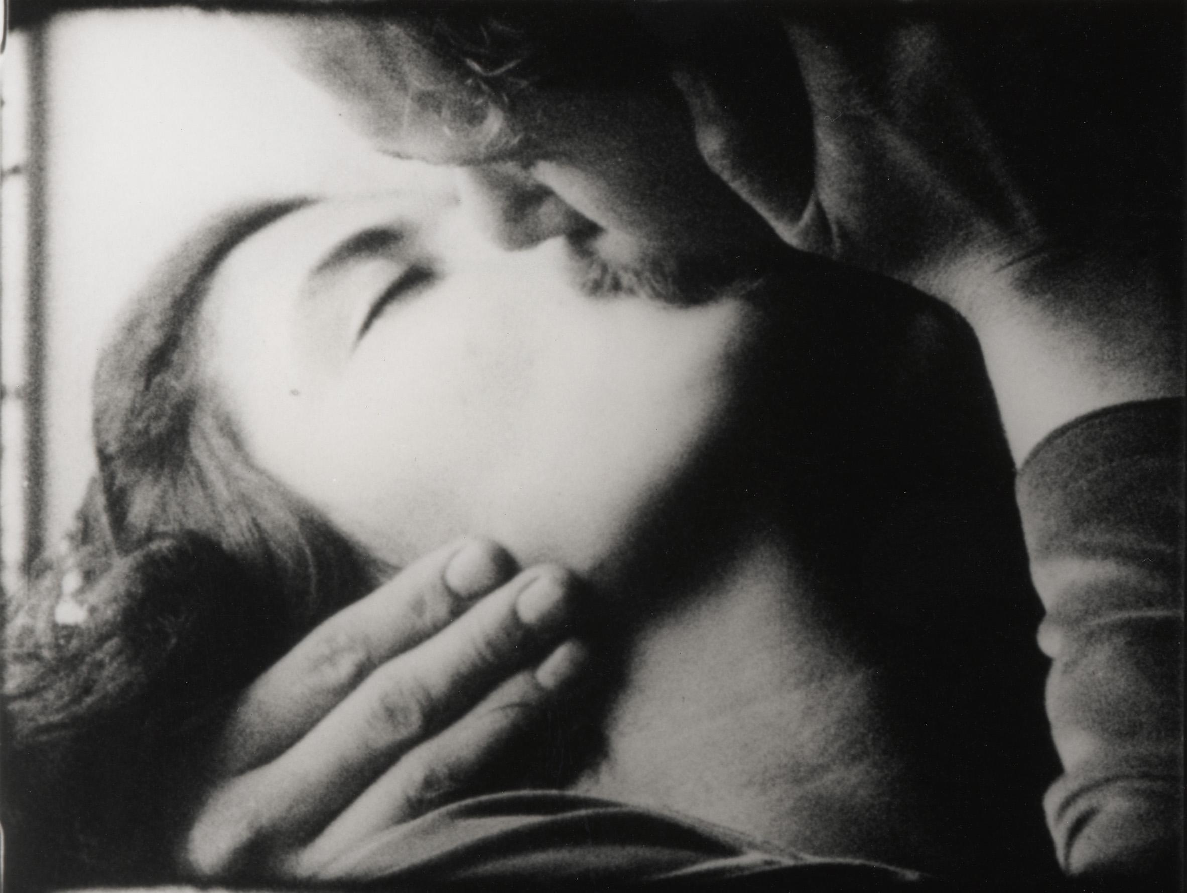 Closely cropped black-and-white photograph of a woman and man kissing, she tilts her head back supported by his hand