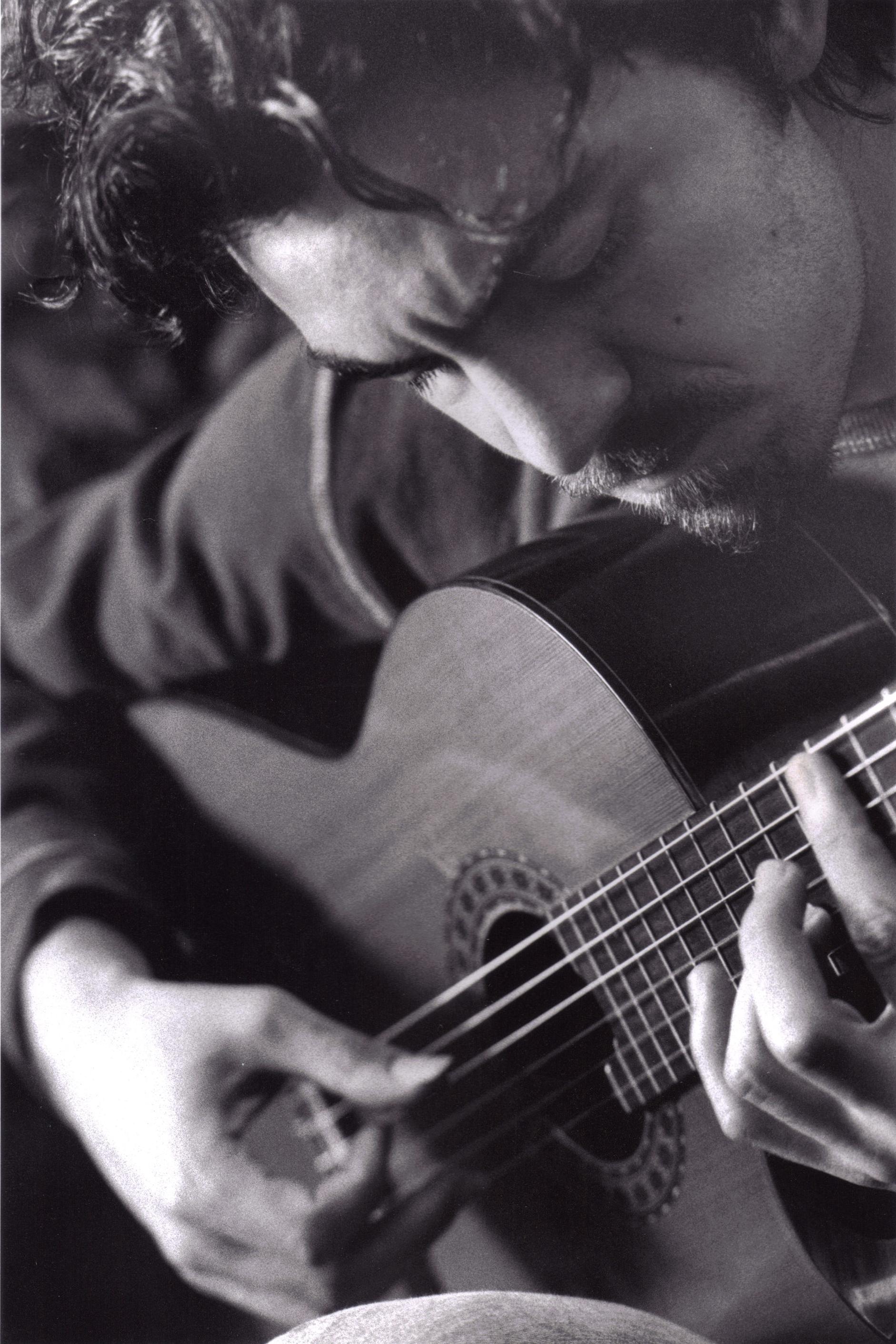 In this black-and-white portrait, a light-skinned male musician plays the guitar.