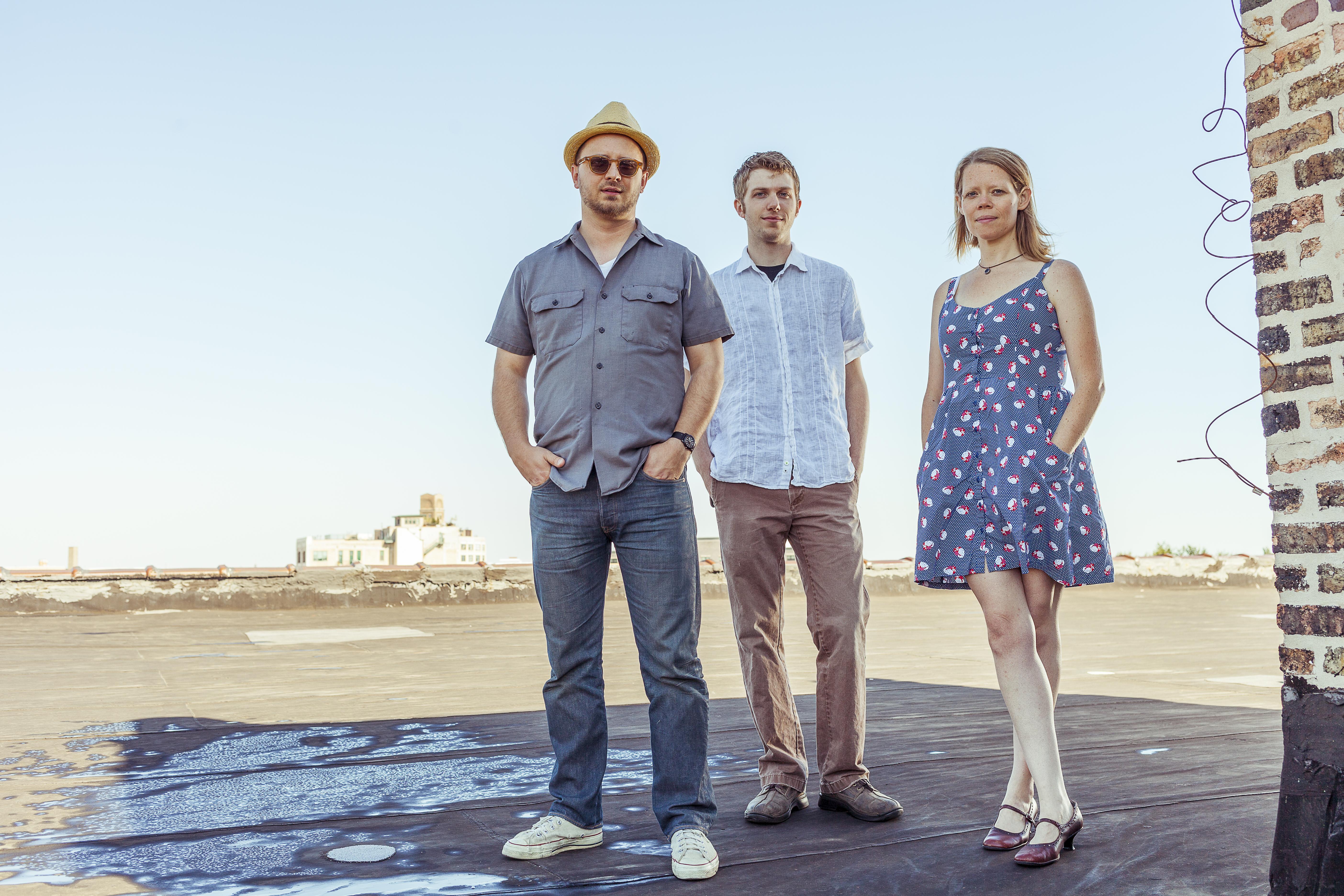 On a sunny day, two men and one woman stand in a shadow cast upon a rooftop.