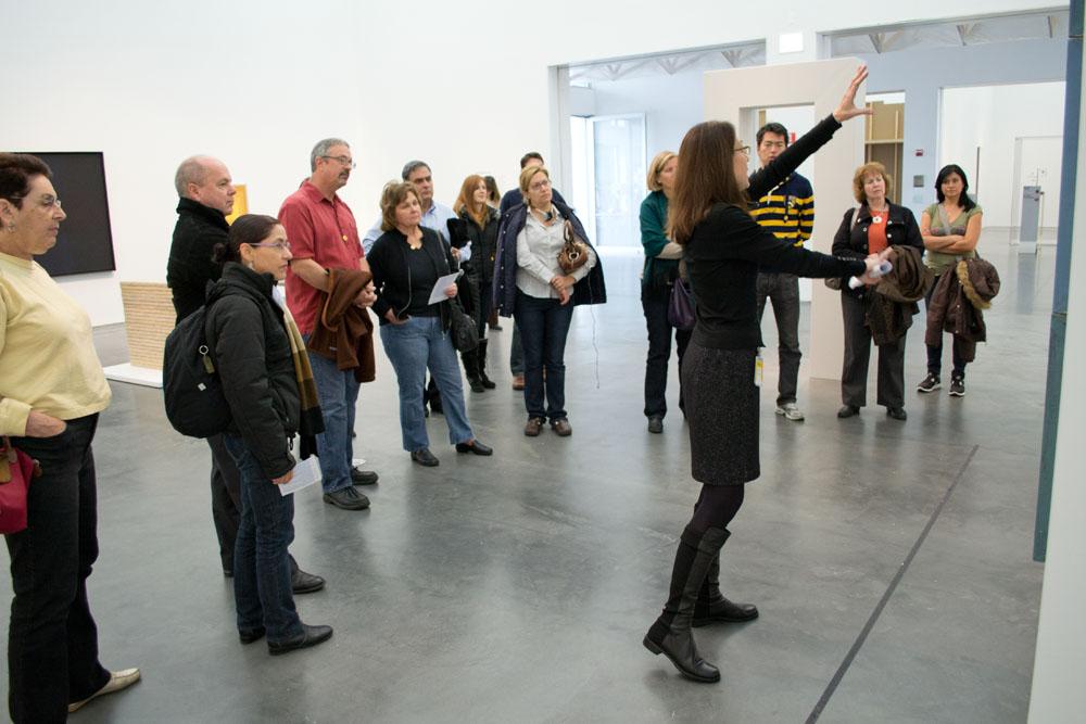 Guide with arms gesturing to a work, surrounded by guests in a gallery