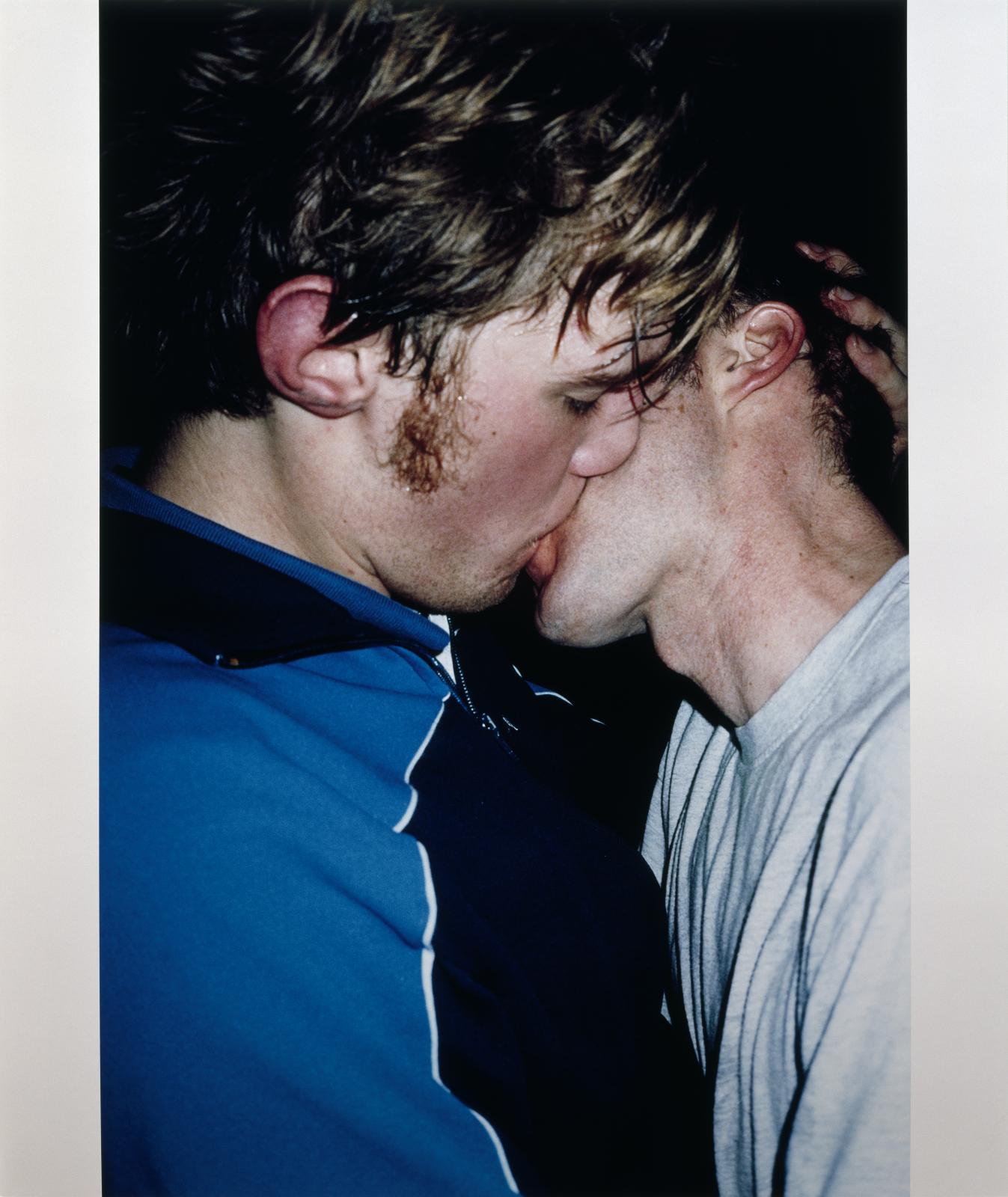 Two pale-skinned, male-presenting people share a kiss.