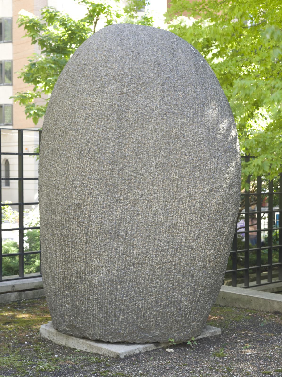 Photograph of a person-sized rounded outdoor sculpture made of grey, textured stone