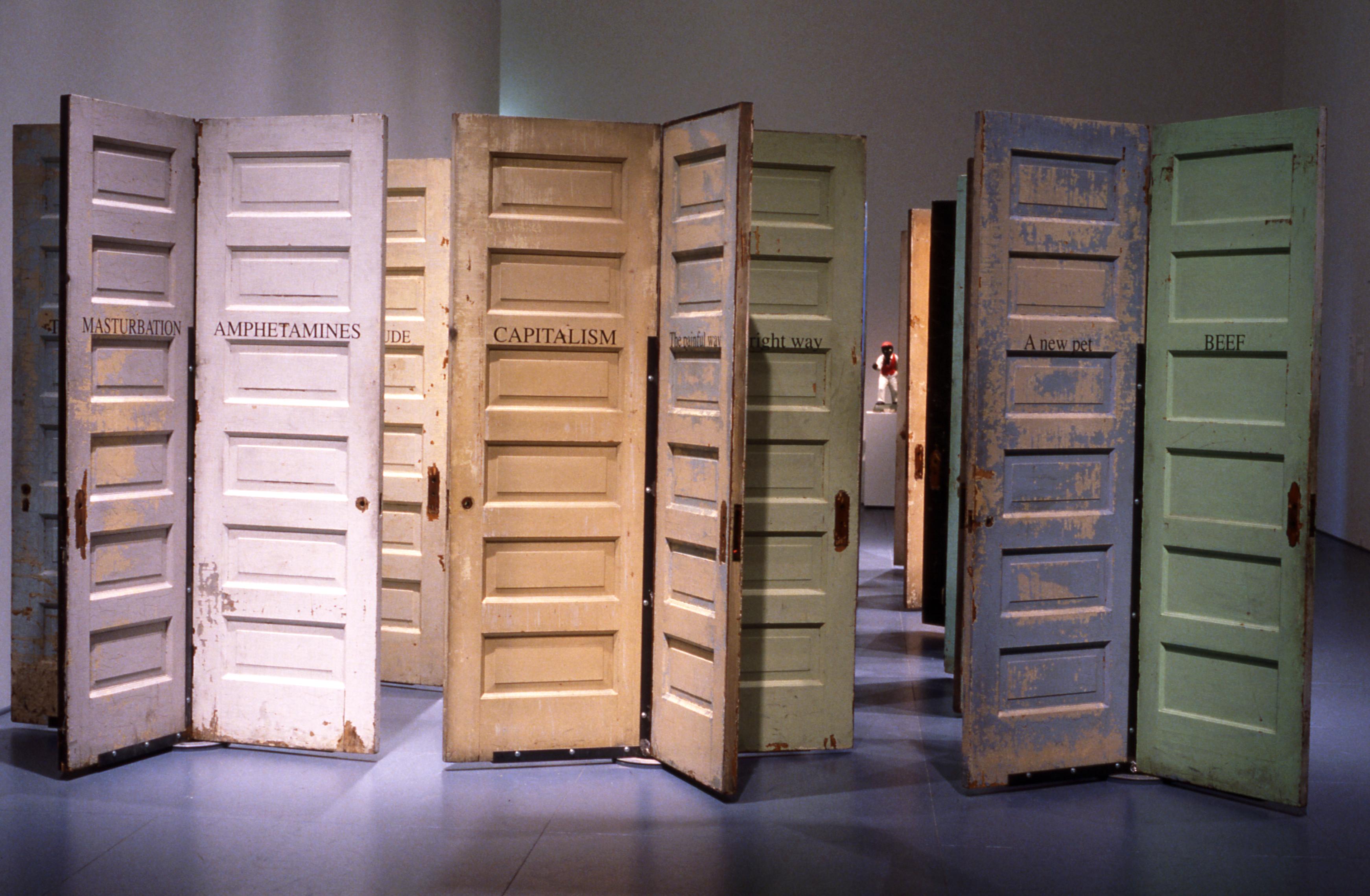 A cluster of pastel-colored doors with peeling paint. Each is labeled with a one-word term, including, "MASTURBATION," "AMPHETAMINES," "CAPITALISM," "BEEF," and "A New Pet."