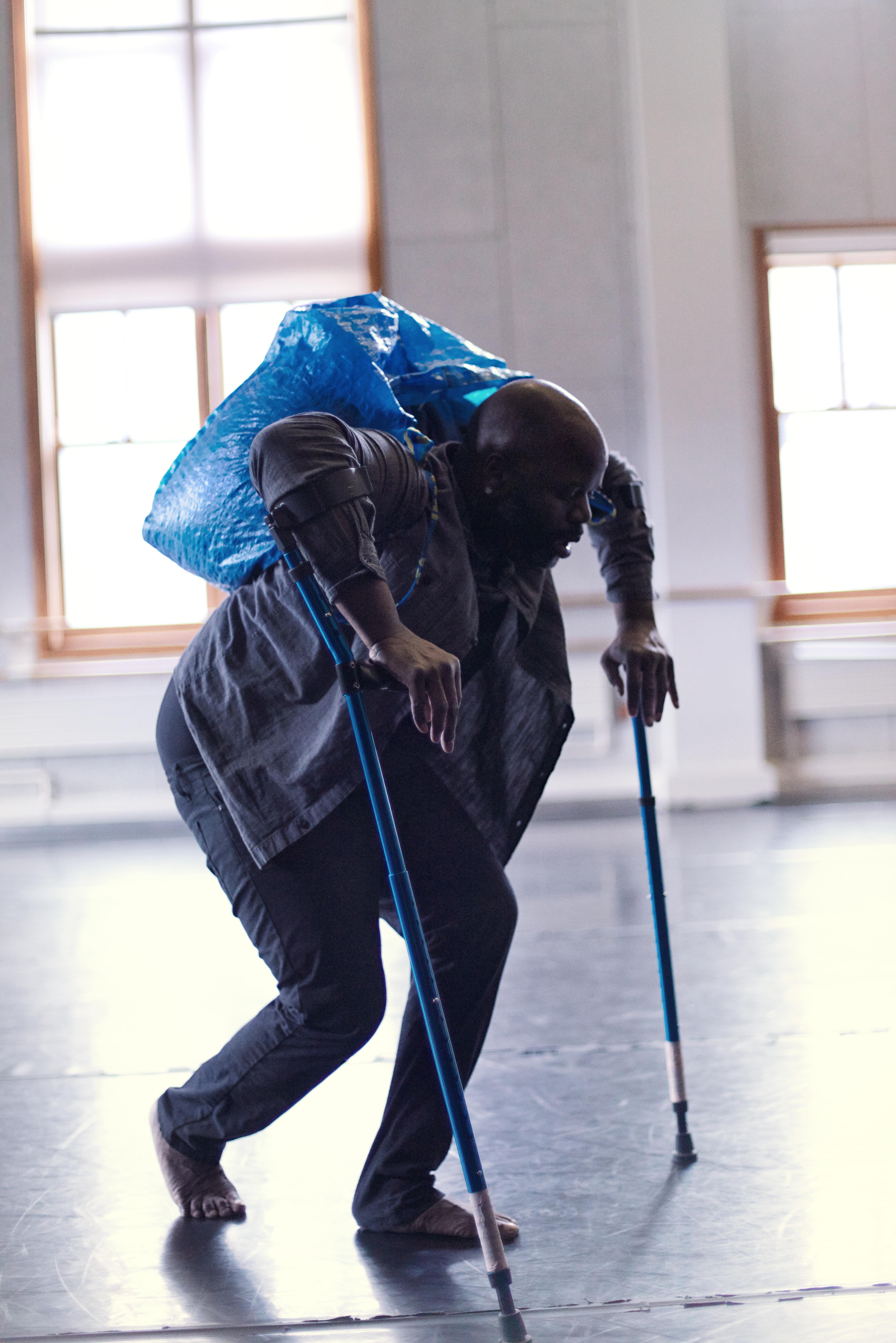 Man in studio dancing while using forearm crutches and wearing a large bag on his back