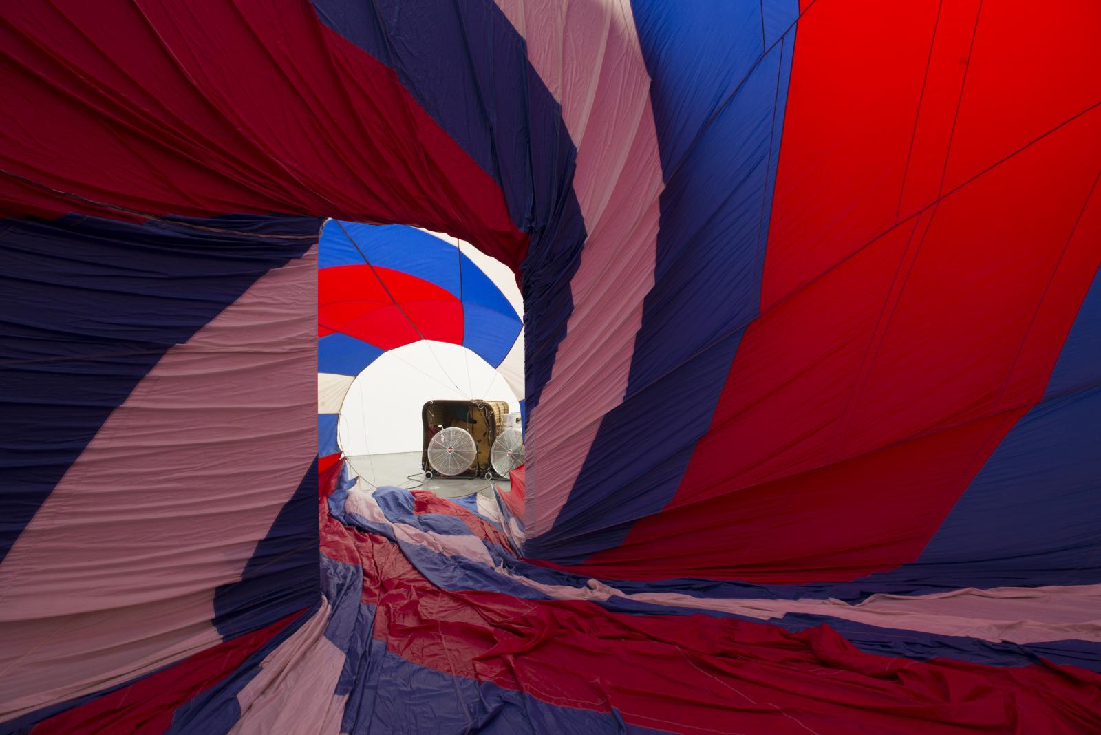 A red, white, and blue fabric canopy presses against walls of room in a spiral; portable fans blow air into the room through a doorway.