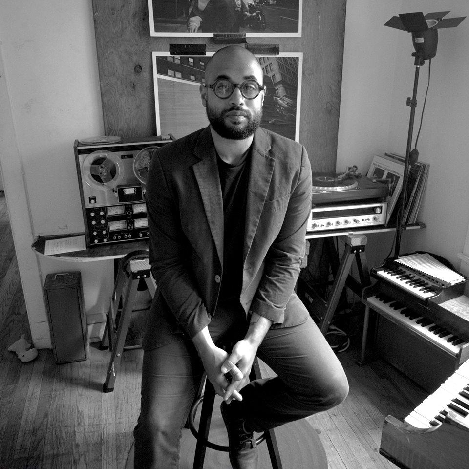 Black and white portrait of Mikel Patrick Avery surrounded by recording equipment