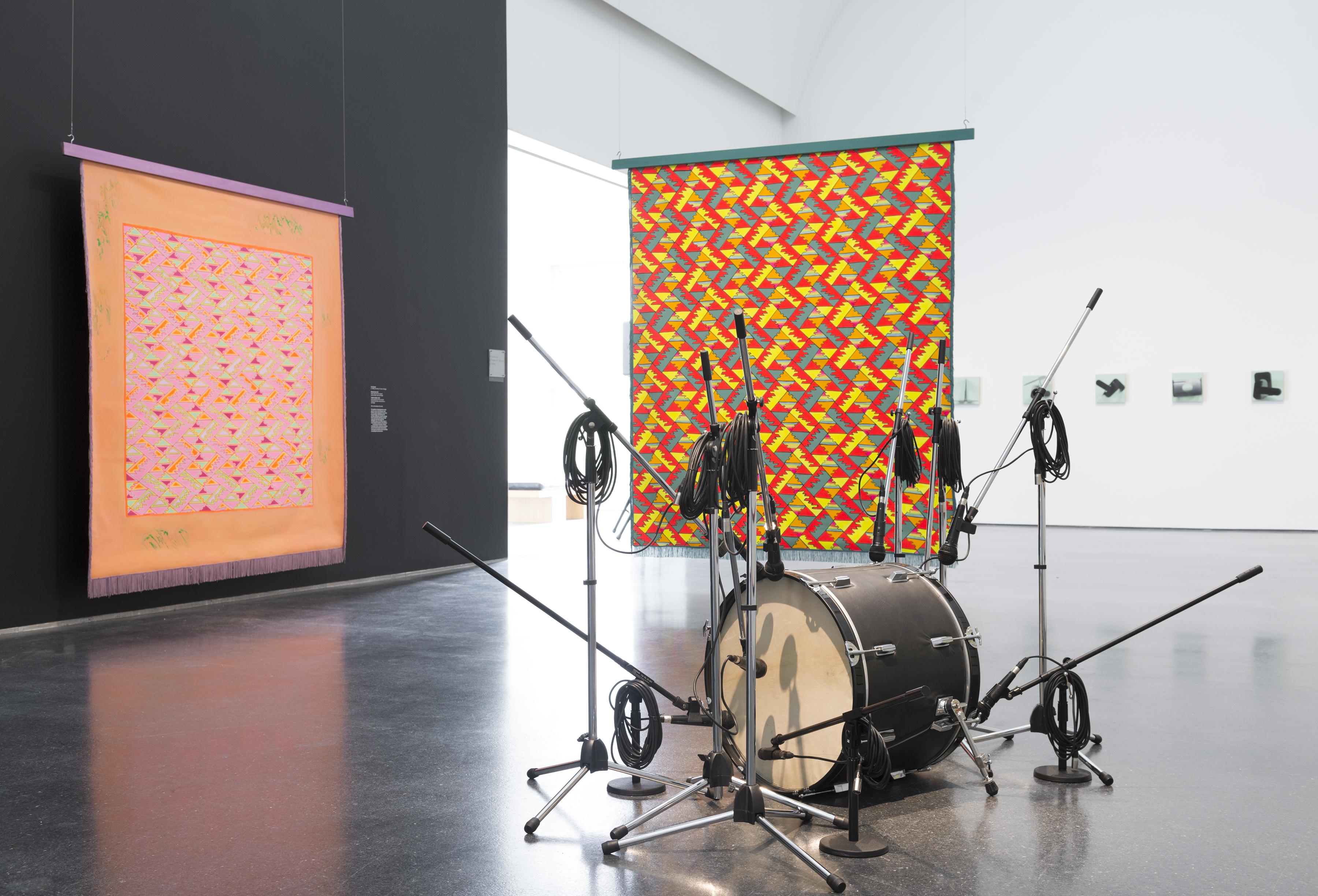 A bass drum surrounded by microphones on stands in front of brightly colored suspended backdrops