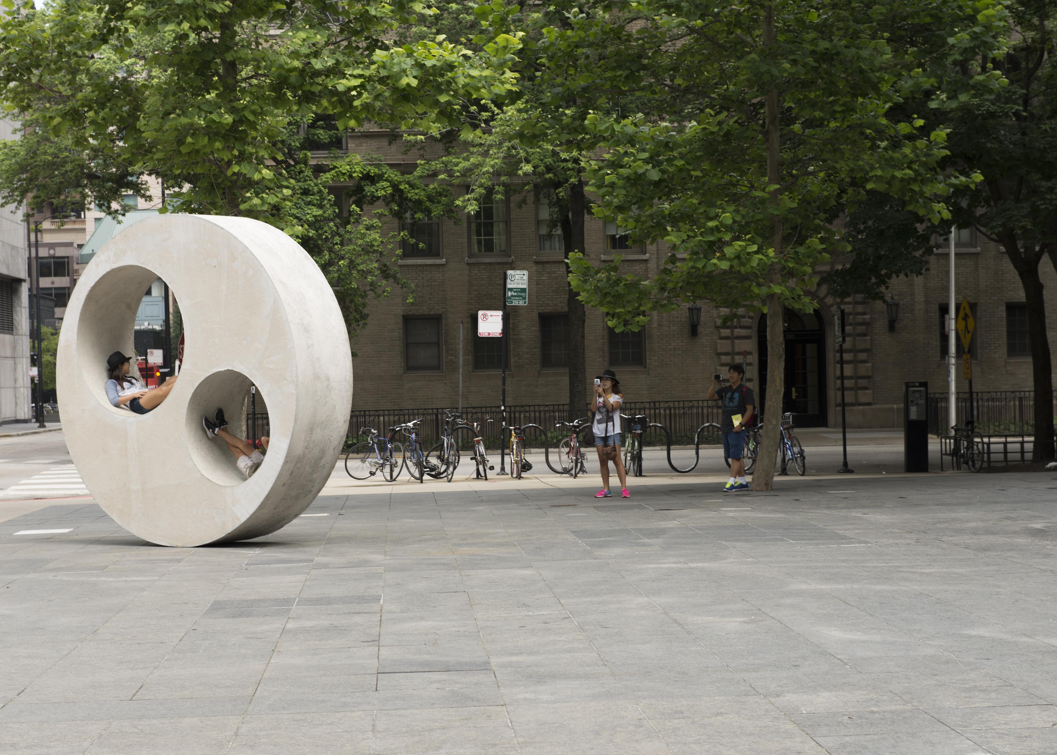 Teens lounging in two circle cutouts of a large circular concrete sculpture on the MCA Plaza