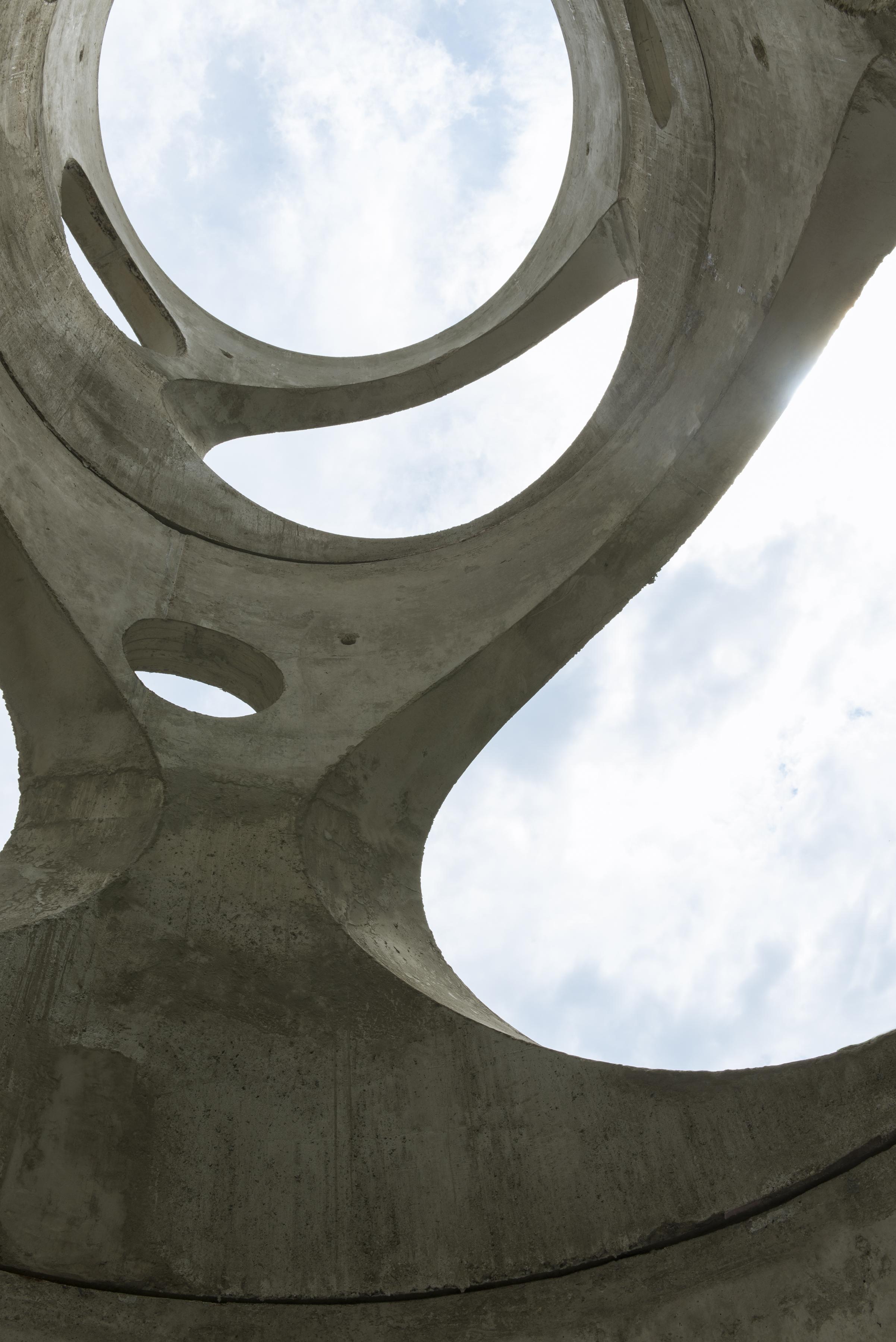 View of a bright cloudy sky through a cylindrical concrete sculpture with circle cutouts