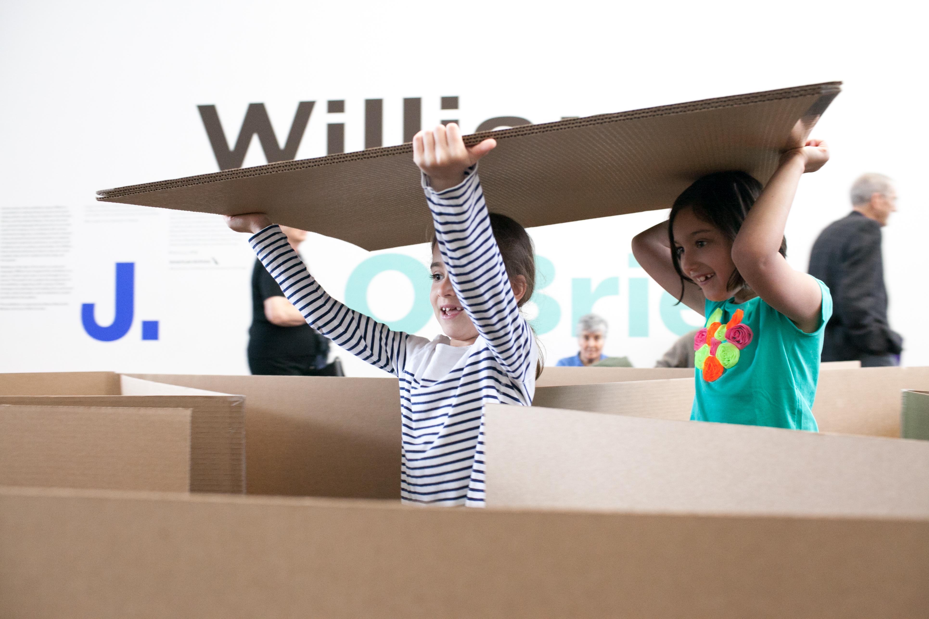 Two girls carrying cardboard sheet through a cardboard maze