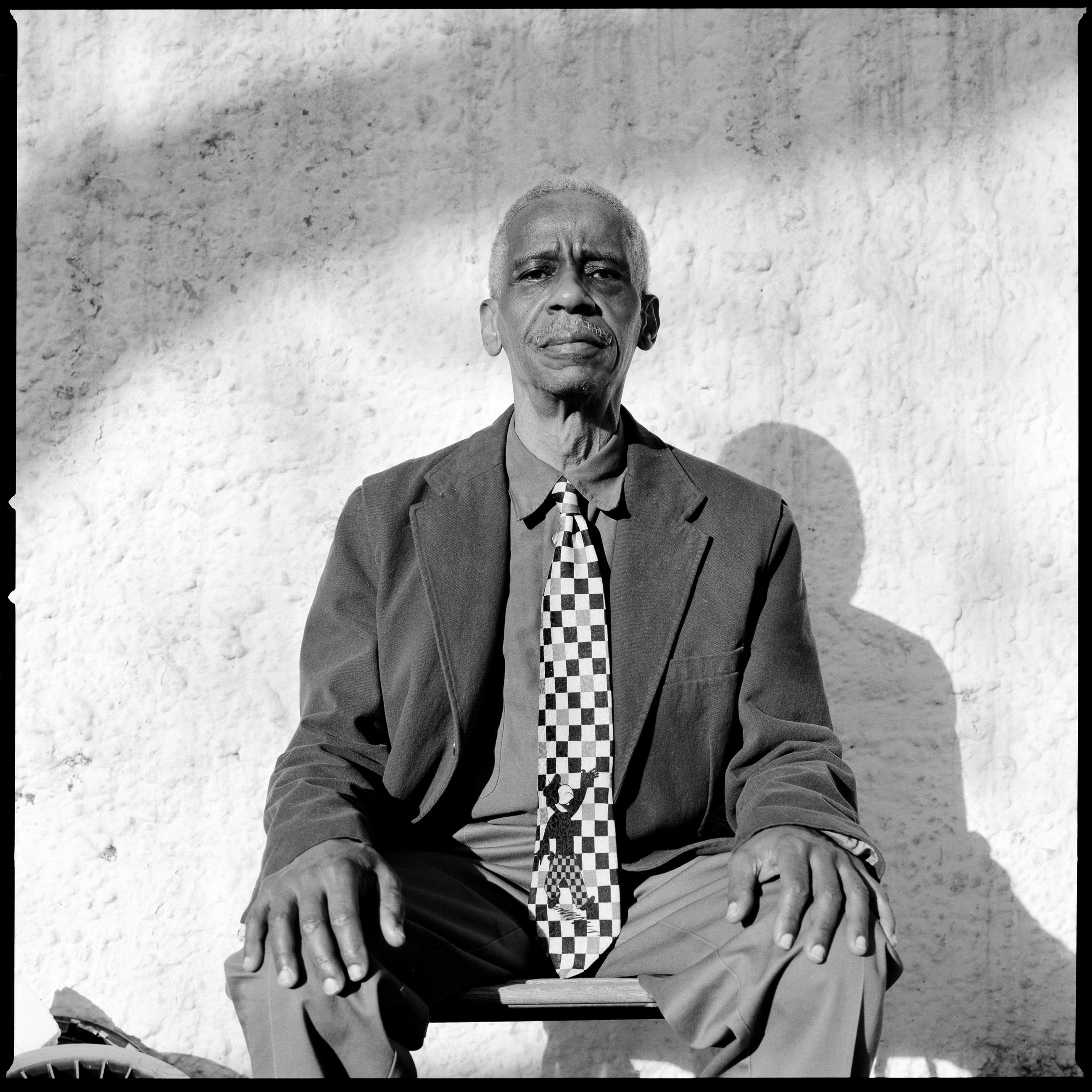 A black-and-white portrait of Roscoe Mitchell sitting on a chair.