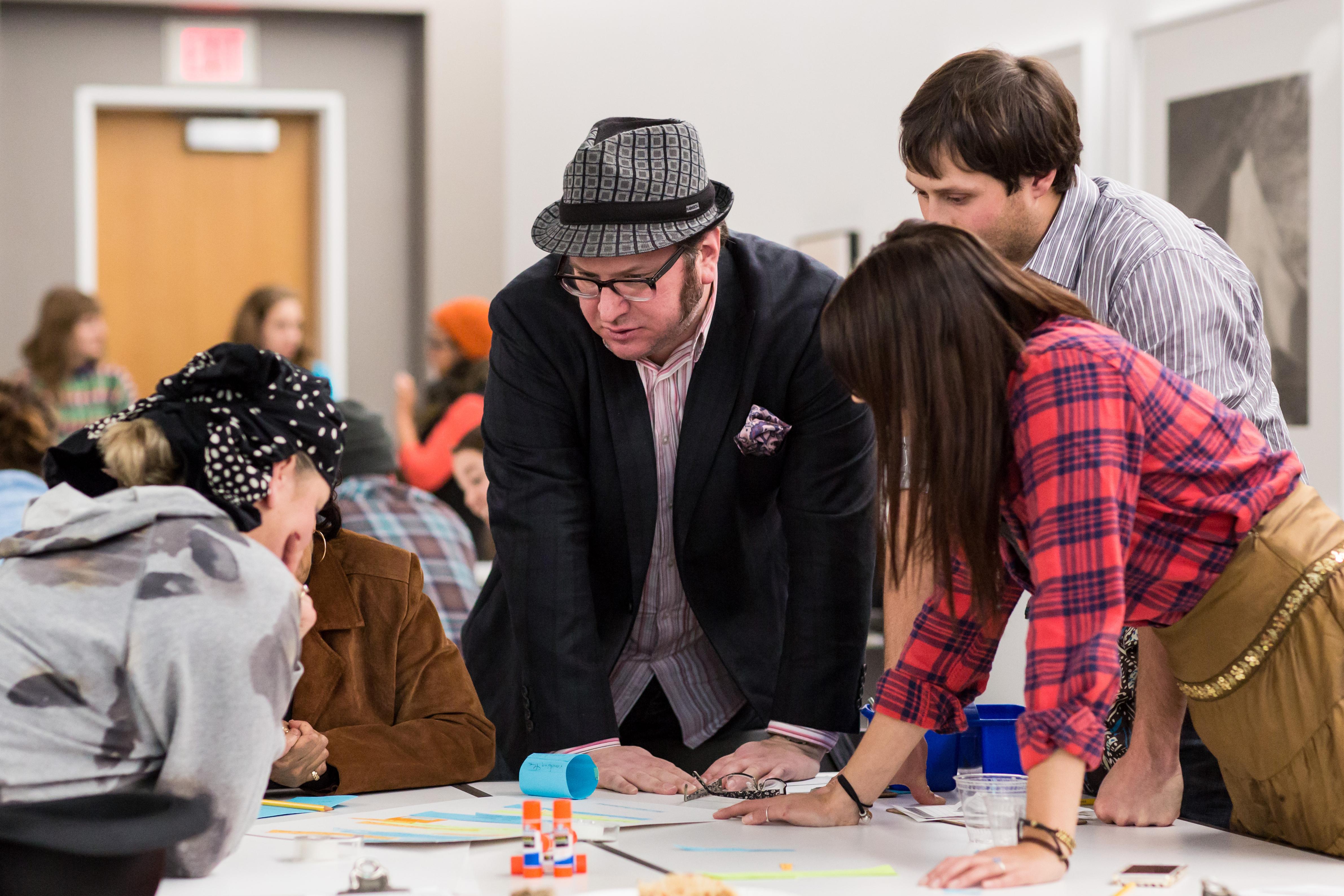 People in discussion lean over a table covered with papers.