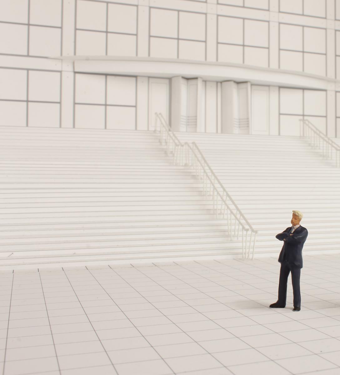 A black-and-white model of the MCA's front staircase with a male figurine in a black suit standing on the plaza.