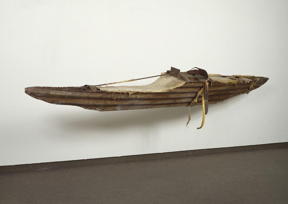 A sculpture in the form of a small canoe is mounted to the gallery wall
