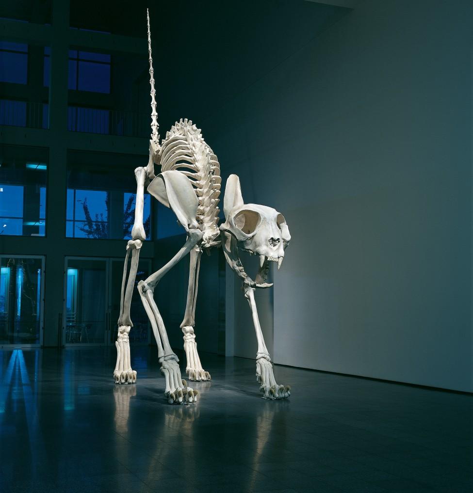 A gigantic cat skeleton stands with its back arched and tail pointed straight up in the air.