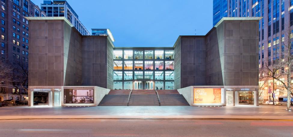 The front of the MCA is lit up at dusk, photographed from across Mies van der Rohe Street.