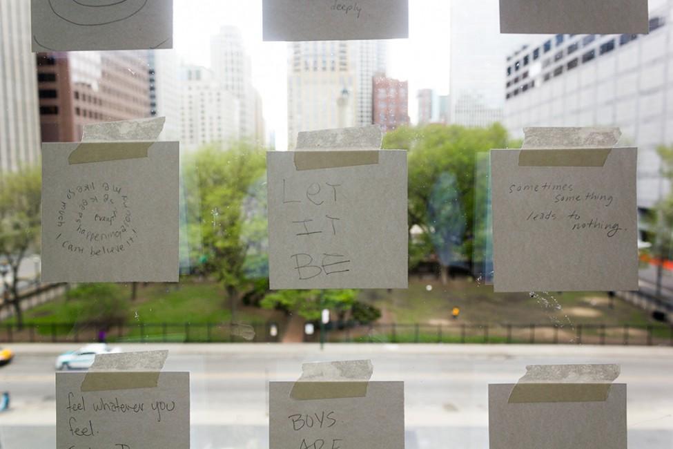 A three-by-three grid of white post-it notes with text taped to the front window of the MCA