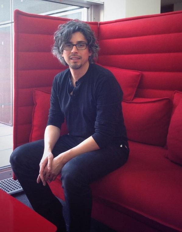 A man with wavy grey hair and glasses sitting on a high-backed red couch