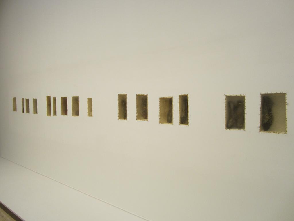 A wall displays several rectangular inlays with shoes inside of them, as if held in amber.