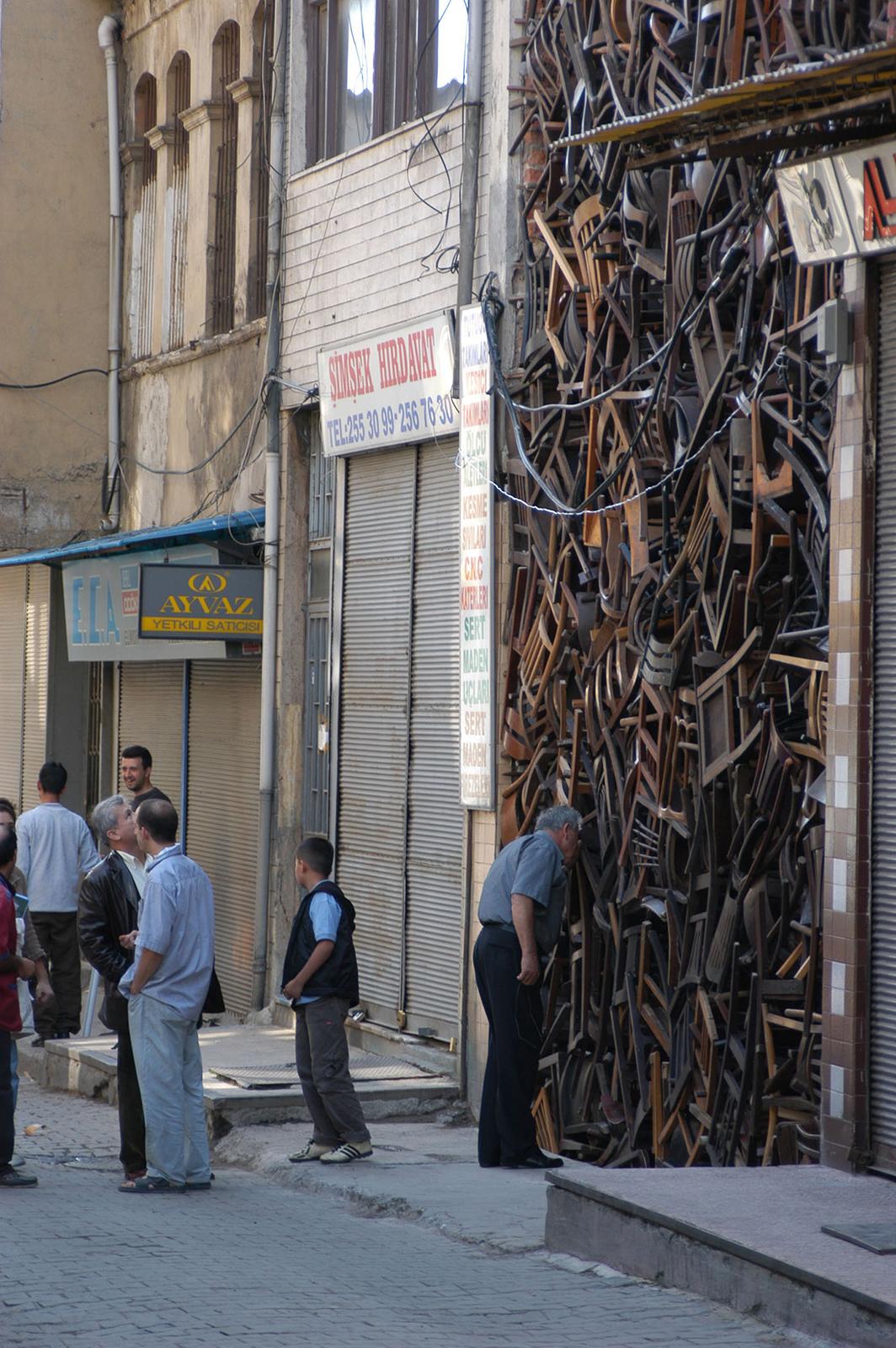 A man bends forward for a closer look at hundreds of stacked wooden chairs filling an alley.