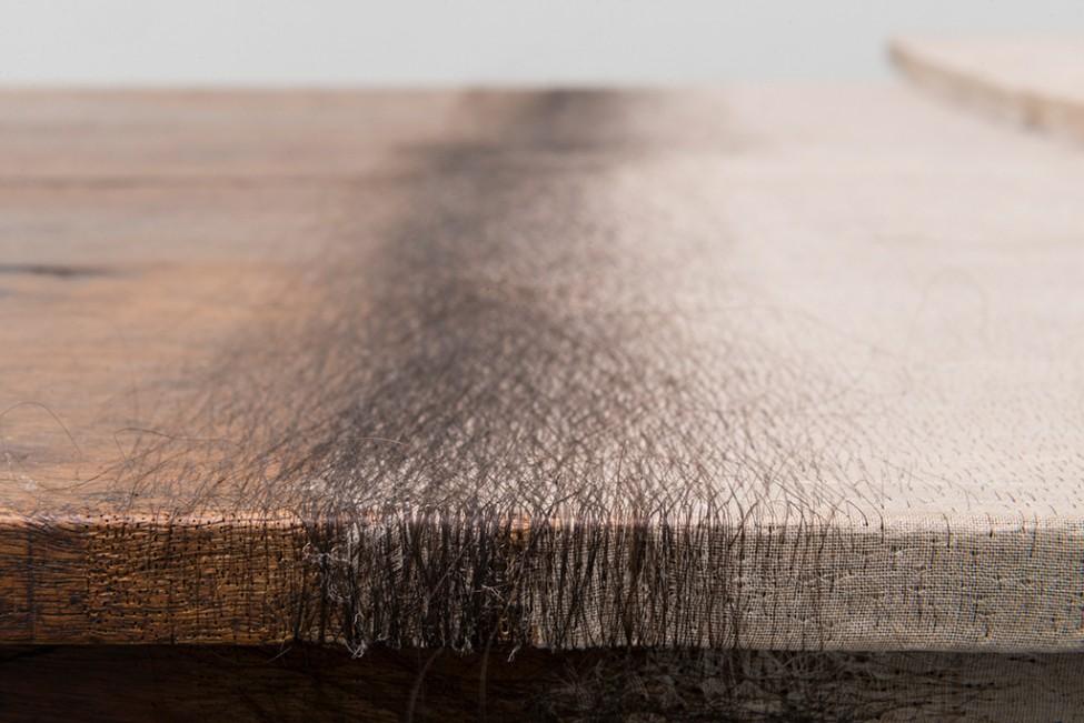 A close-up photograph shows a wooden table with the interwoven pattern of hair delicately matted into it.