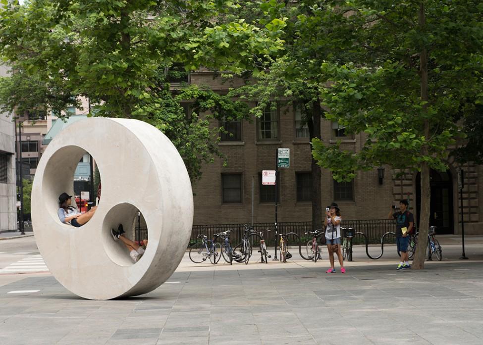 Teens lounging in two circle cutouts of a large circular concrete sculpture on the MCA Plaza