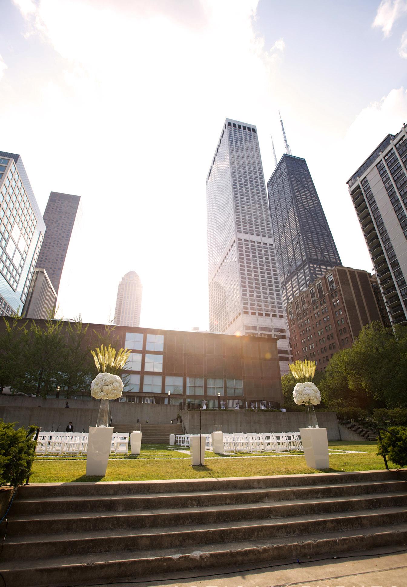 A view of the MCA's sculpture garden and terrace on sunny day is set with white chairs for what appears to be a wedding ceremony.