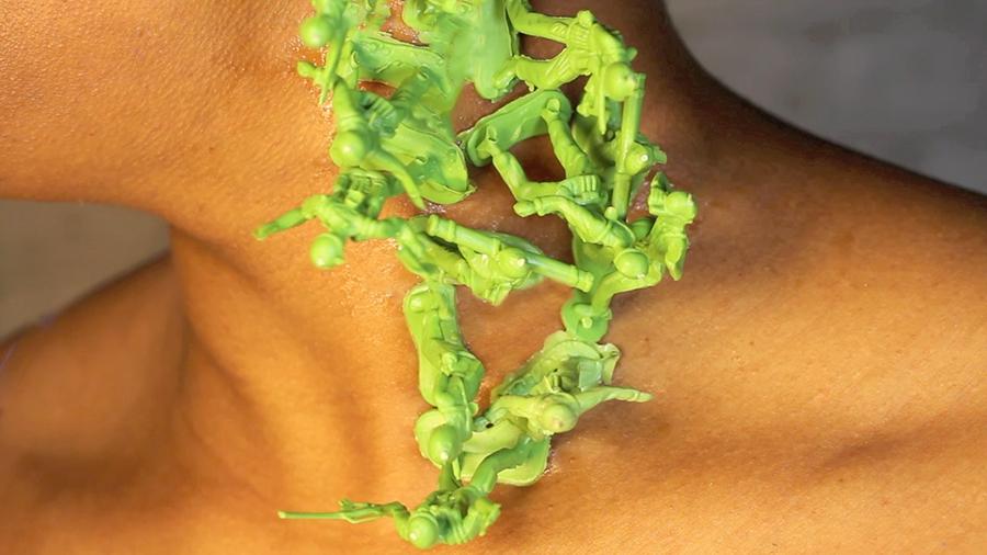 A close-up shows a cluster of lime green army figurines melted to the side of a person's neck.