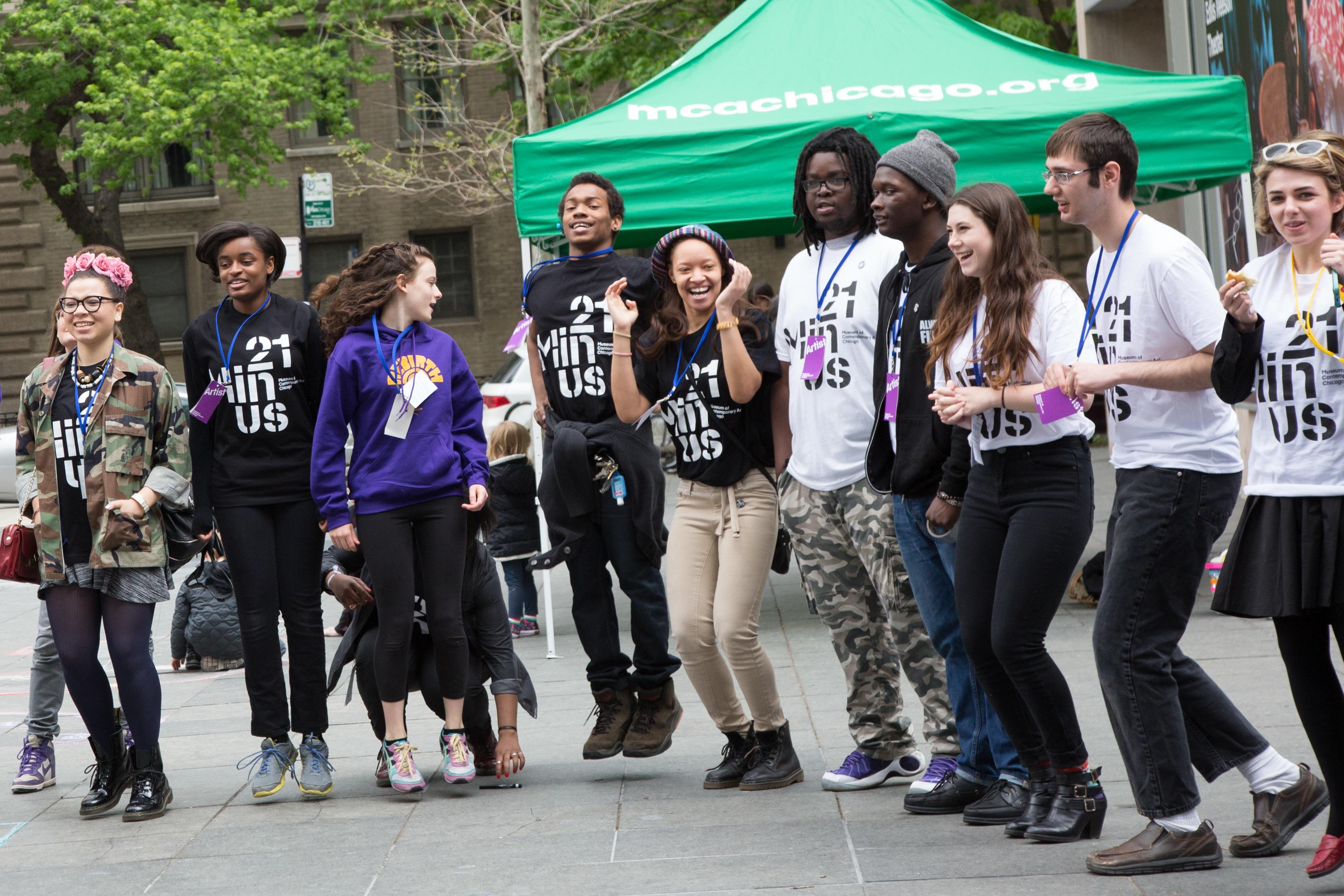 A group of ten Chicago teens jump excitedly on the MCA plaza, each of them wearing a 21 Minus T-shirt.