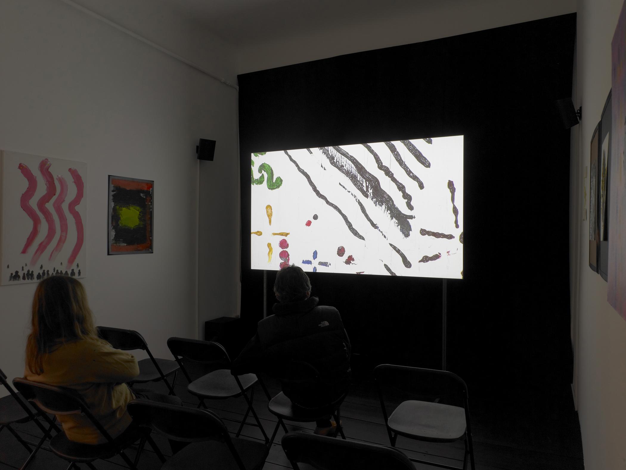 Two audience members watch a video projection of abstract painted lines on a white background in a dark room with paintings
