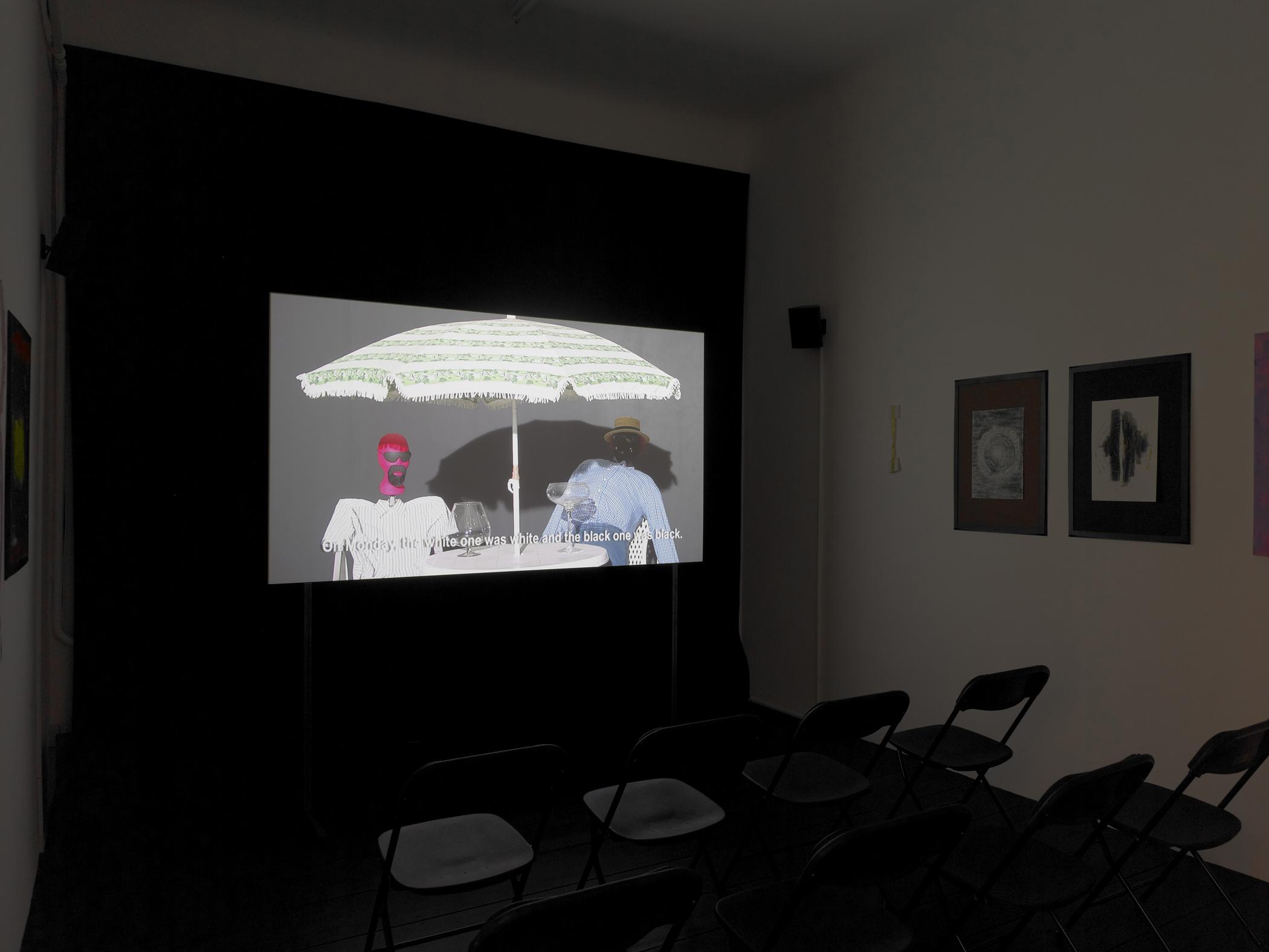 Installation view of a video projection of two humanoid dolls sitting at a table shaded by a striped umbrella