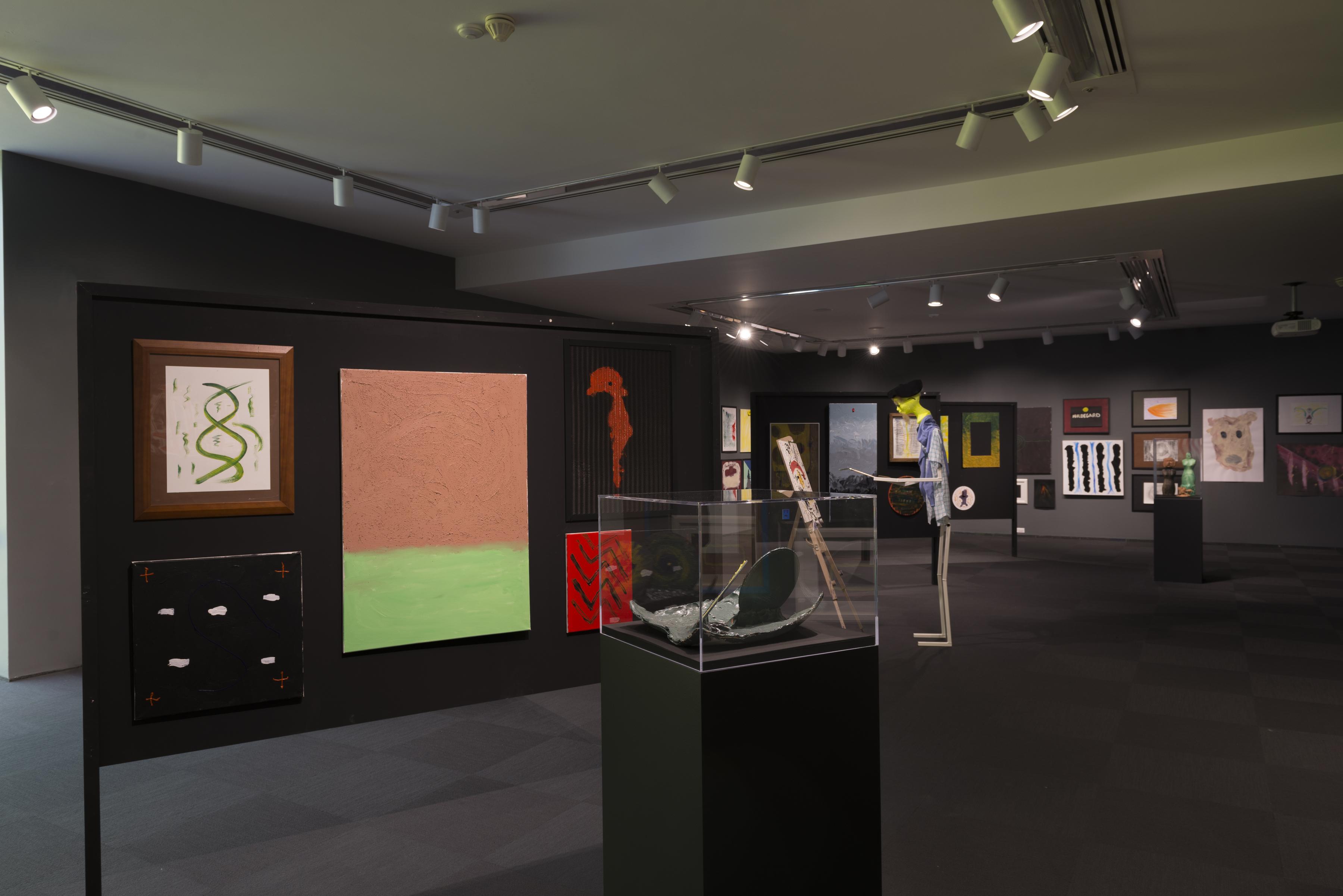 A humanoid figure with a yellow head stands in front of an easel and canvas in the middle of a dark grey gallery with paintings hung in clusters and sculptures on pedestals.