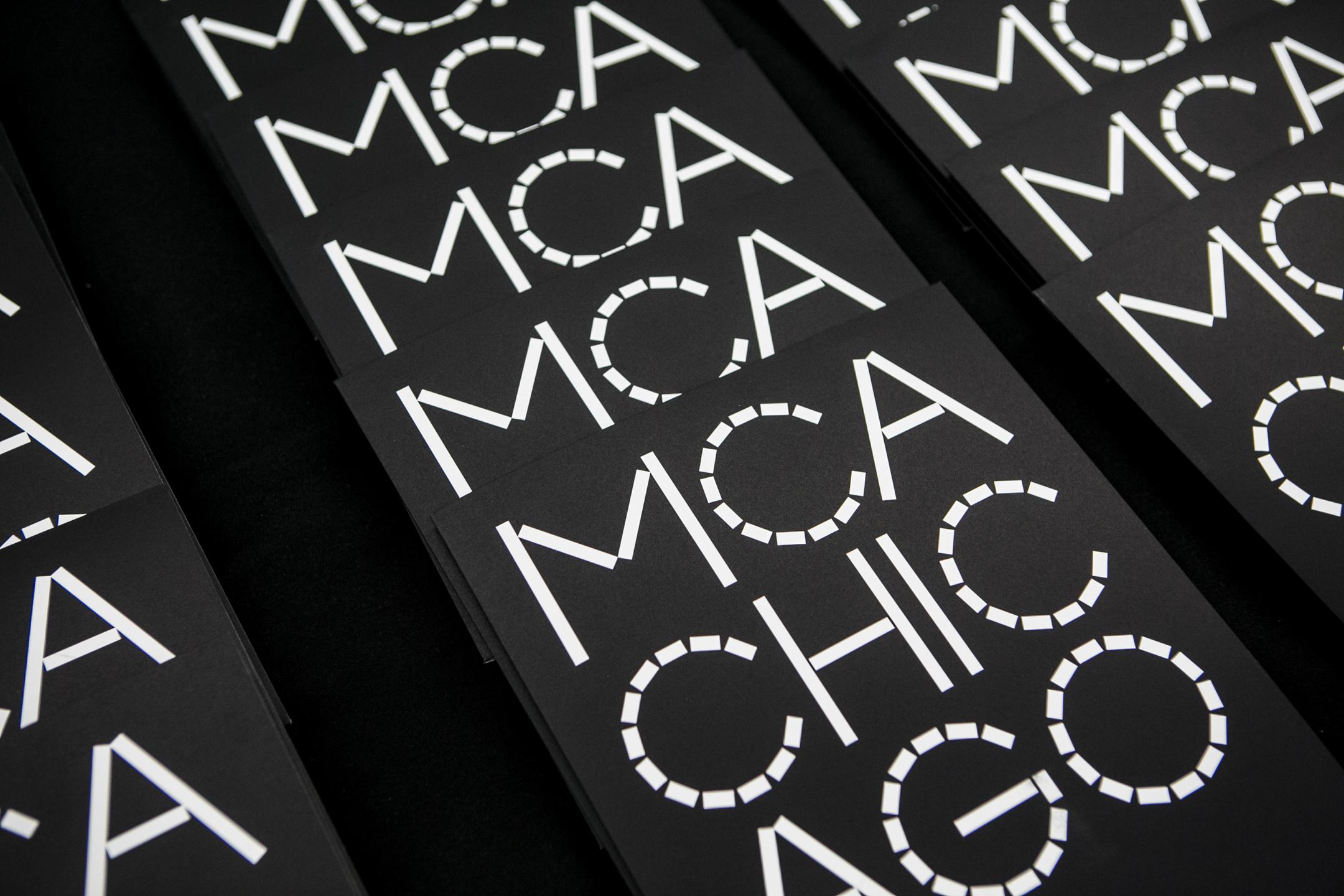 Rows of black folders with a white logo that reads "MCA-CHIC-AGO" are lined up to repeat "MCA."