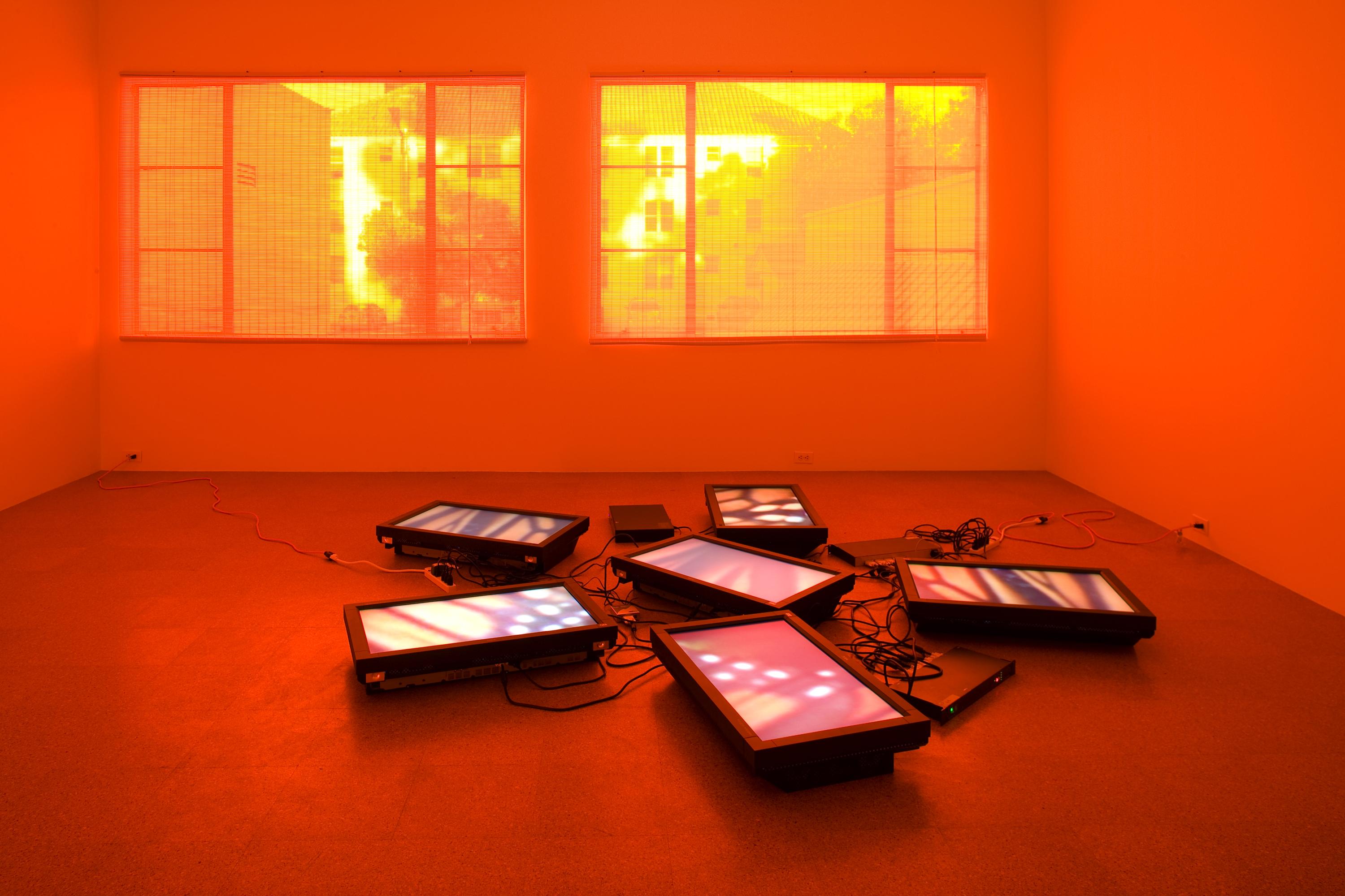 A room, lit up bright orange, contains five flat screen monitors and their cables on the floor. Each screen shows a close-up image of a butterfly wing.