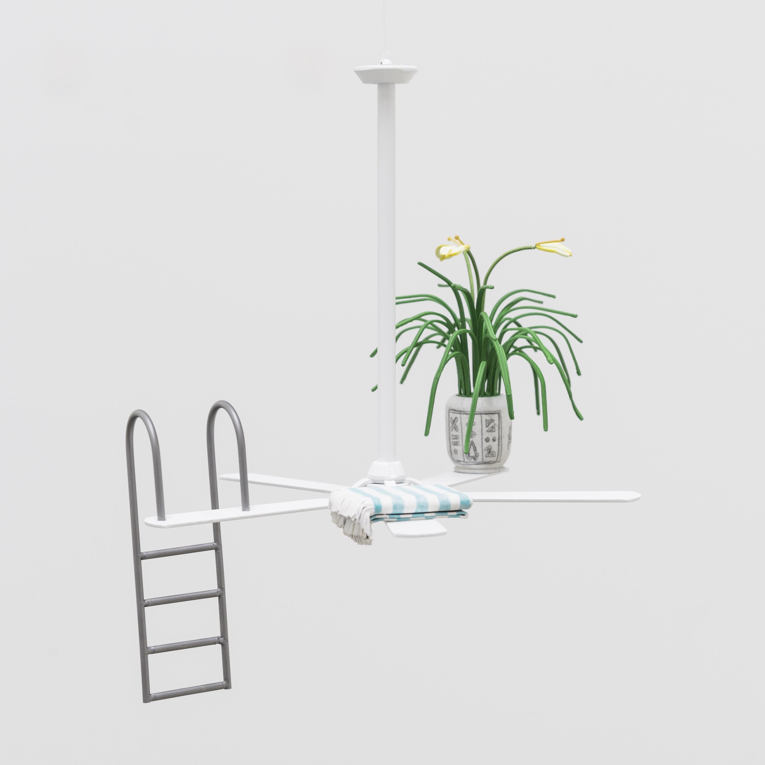 This is a miniature sculpture of a ceiling fan. On three of the fan blades sits three objects: a potted plant, a folded striped linen, and a pool ladder.
