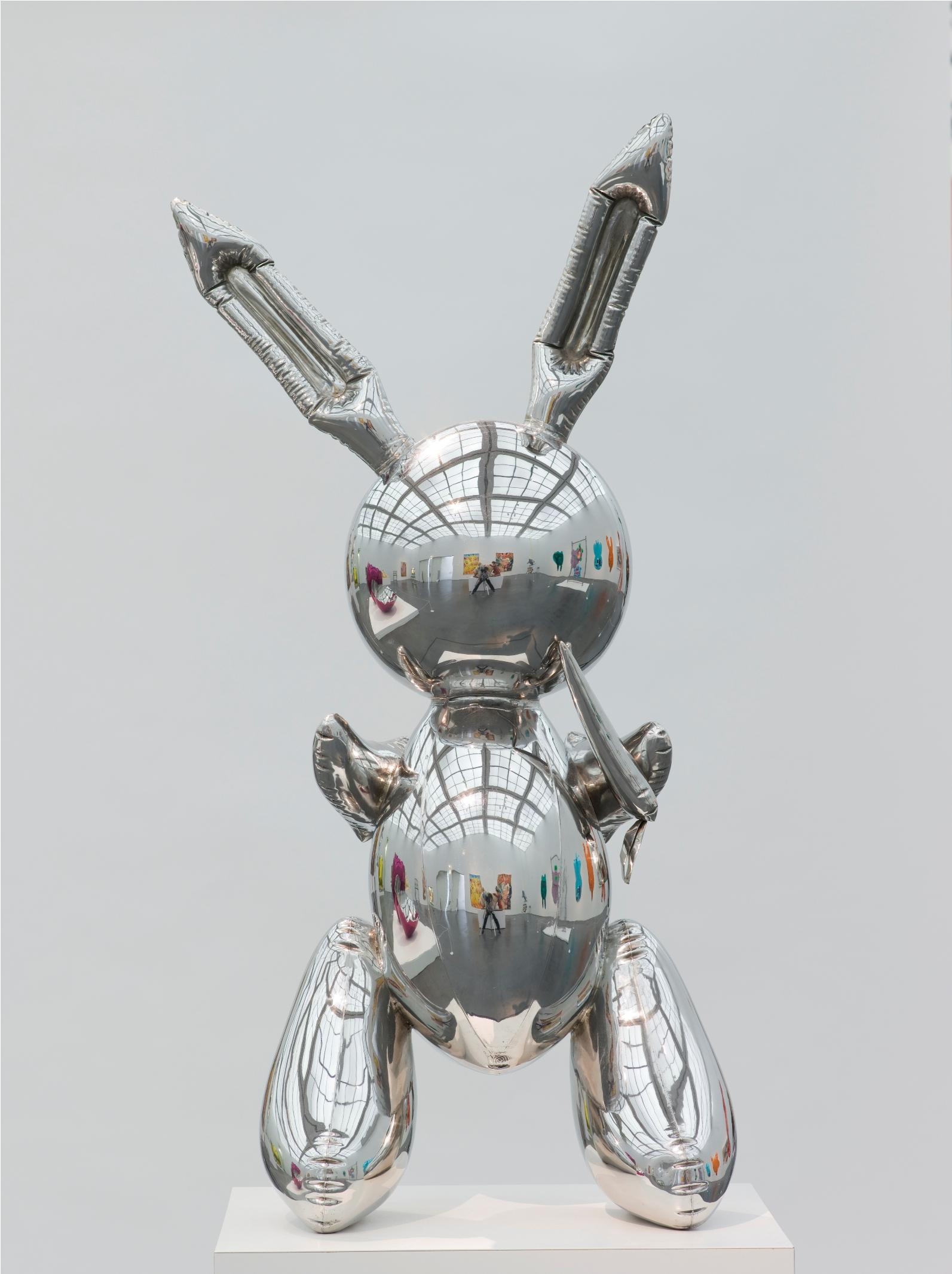 A sculpture that resembles a rabbit-shaped mylar balloon stands on a pedestal. A museum gallery is visible in the sculpture's reflective surface.