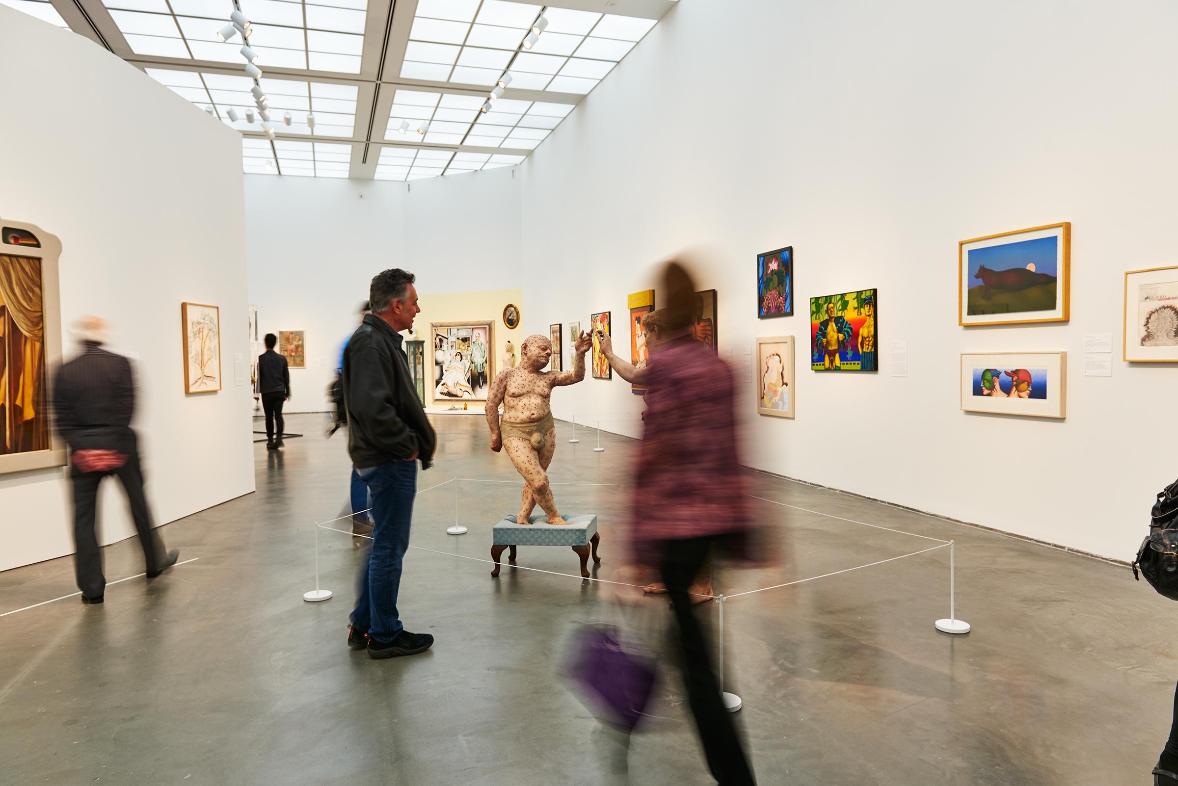 Several visitors look at paintings and sculpture in a gallery whose curvilinear walls draw viewers closer to its center.