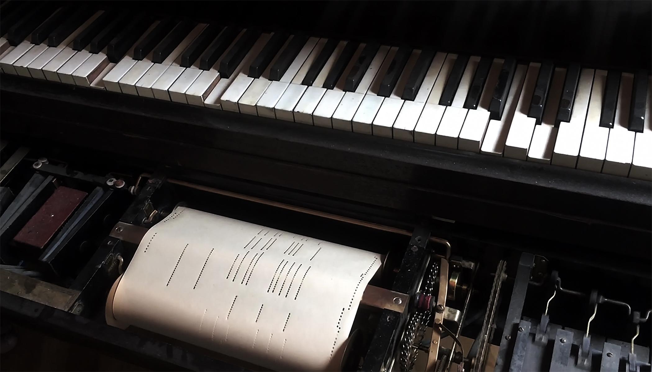 A close-up of a player piano keyboard captures the roll of sheet music mid-song.