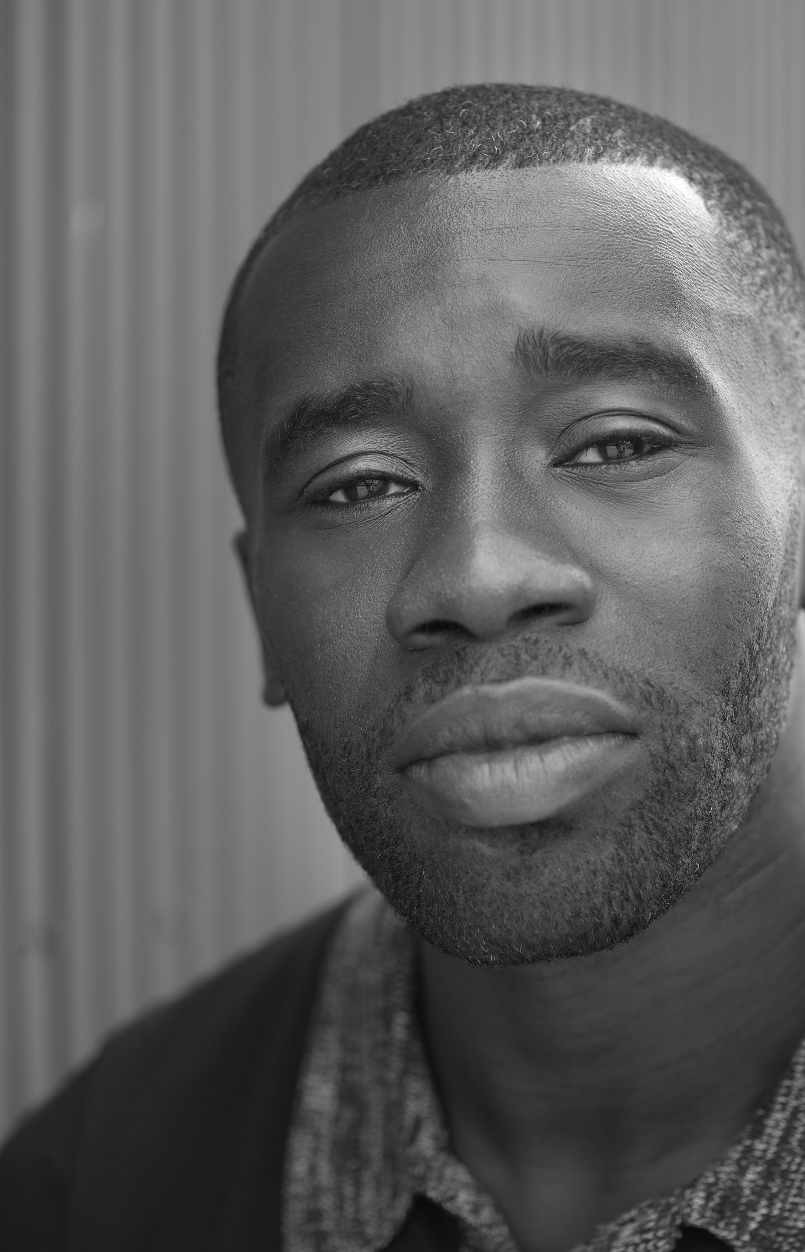 A young black man with a closely shaved head and beard looks directly at the viewer.