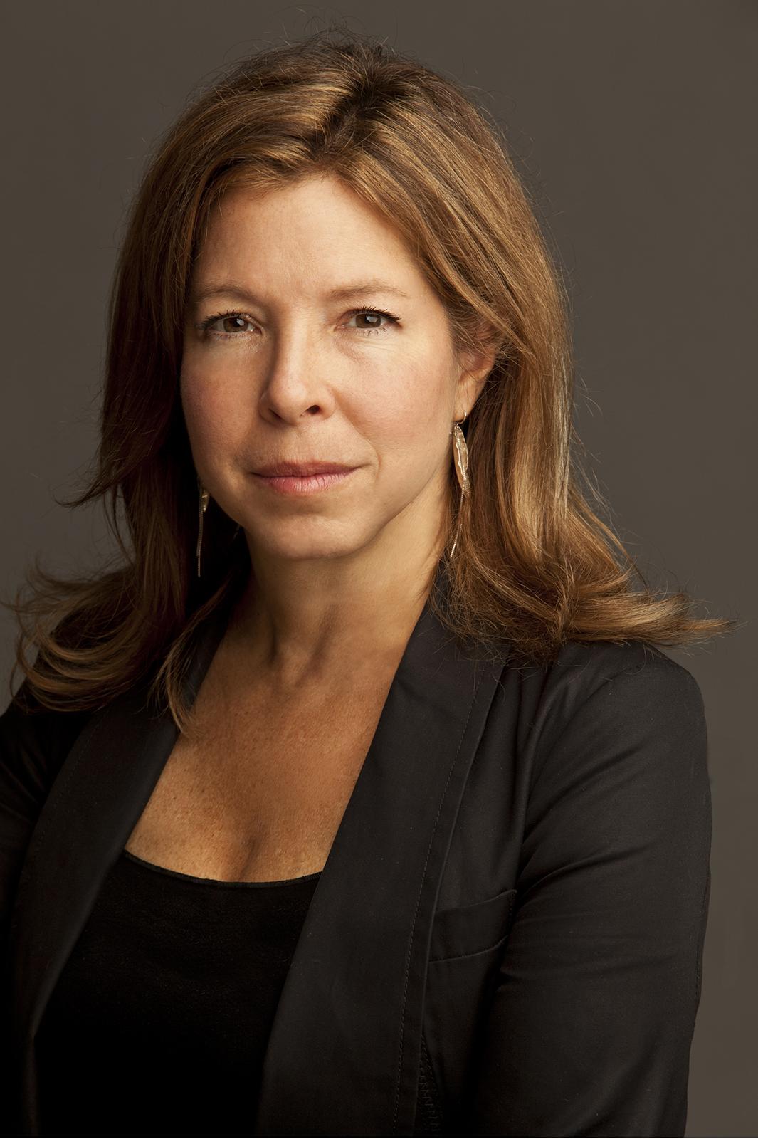 A headshot of a woman with red hair dressed in a black shirt and blazer.